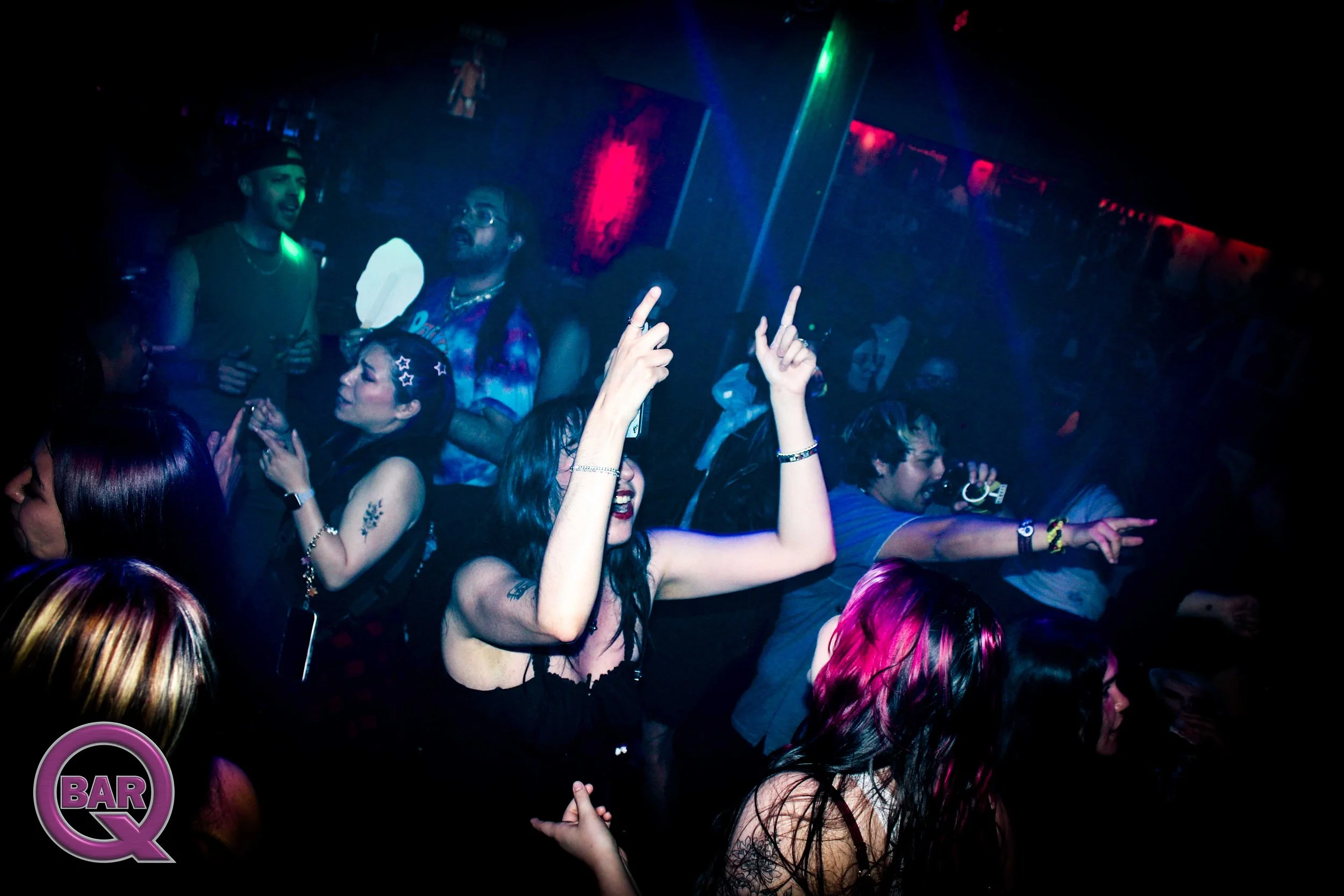 Crowd dancing and singing at a nightclub with colorful lights, raised hands, and a lively atmosphere.