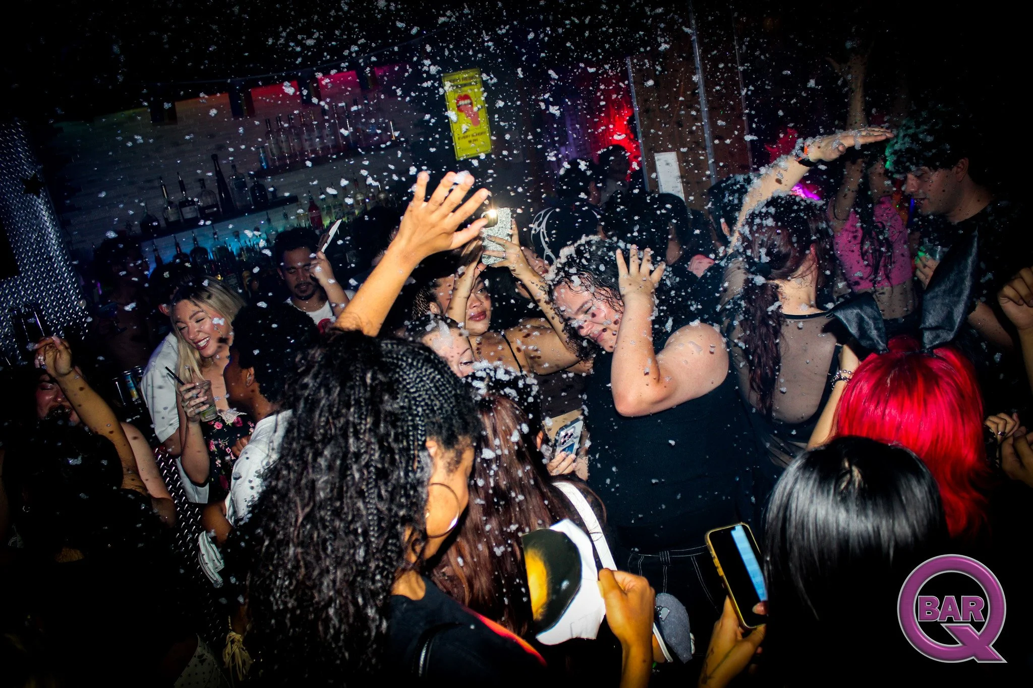 People dancing and having fun at a nightclub with foam and colorful lights.