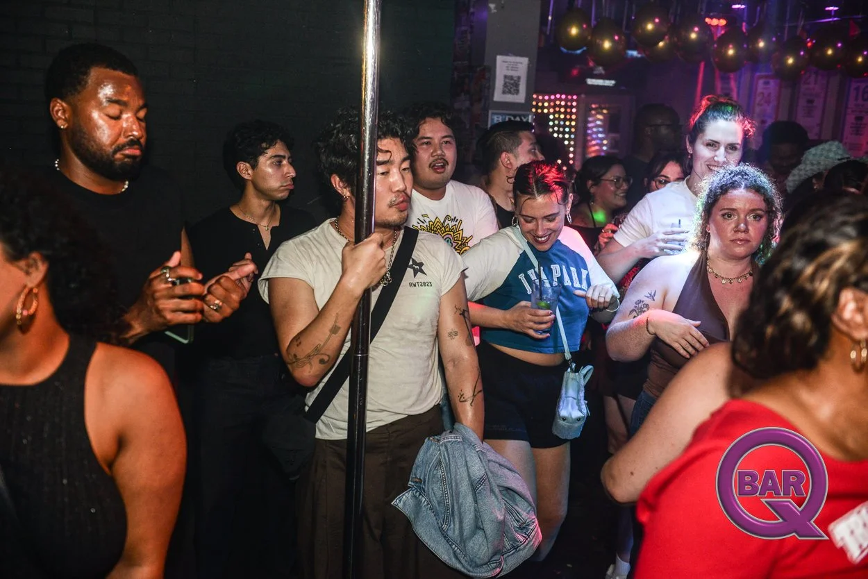 People dancing and enjoying themselves at a bar or club, with colorful lights and balloons in the background.