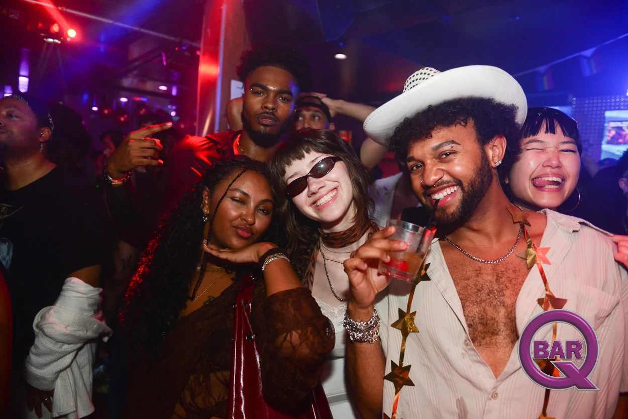 Group of friends celebrating at a bar, with colorful party lighting, smiling, and wearing festive accessories.