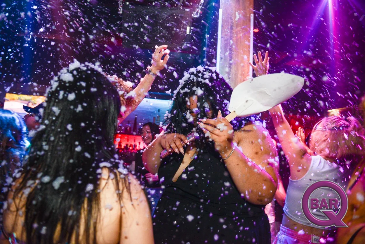 People dancing and having fun in a nightclub with foam and colorful lights.
