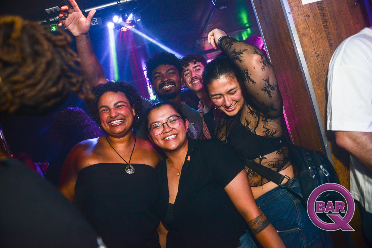 Group of five happy friends dancing and smiling in a nightclub with colorful lights.