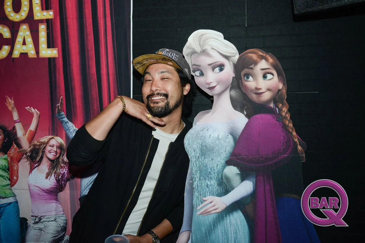 A man posing with cutouts of Disney characters Elsa and Anna from Frozen, at a promotional event.