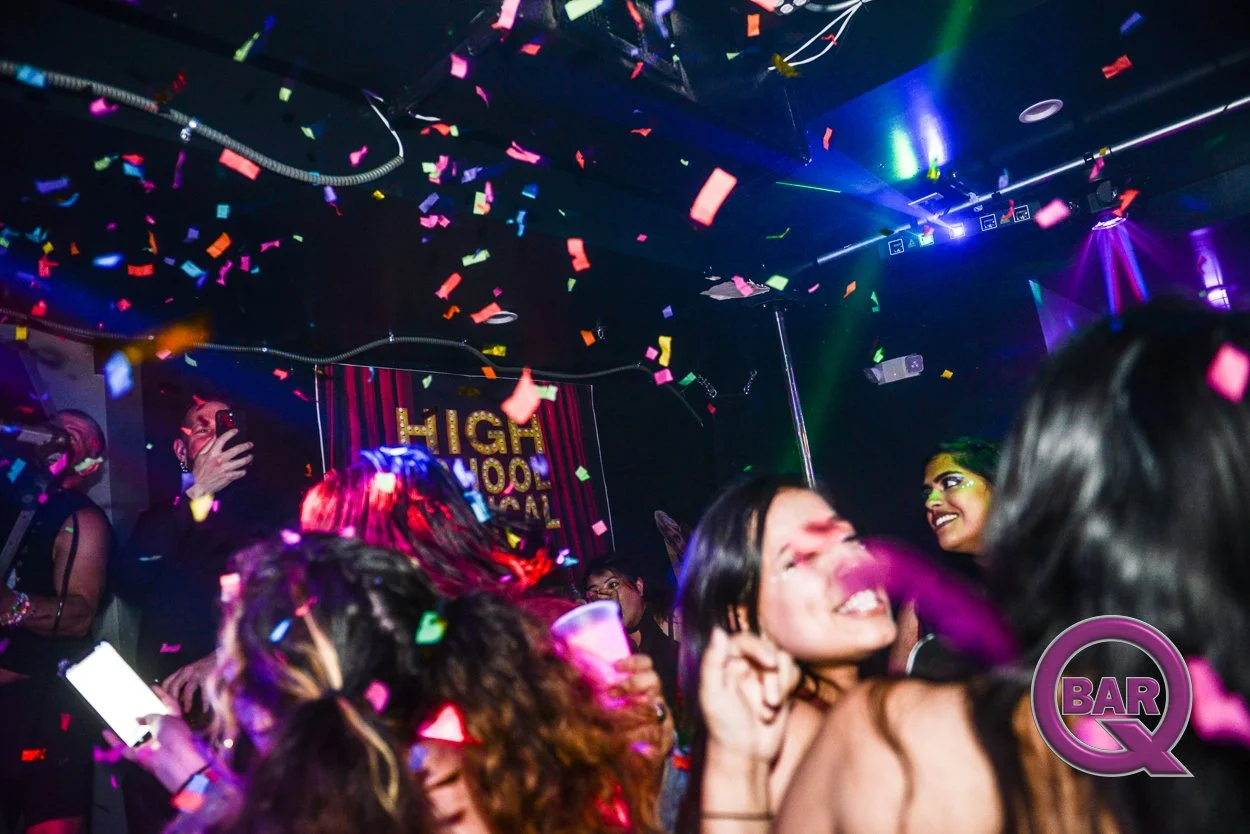 People dancing and celebrating at a nightclub with colorful confetti, bright lighting, and a sign that reads "Highwood Social" in the background.