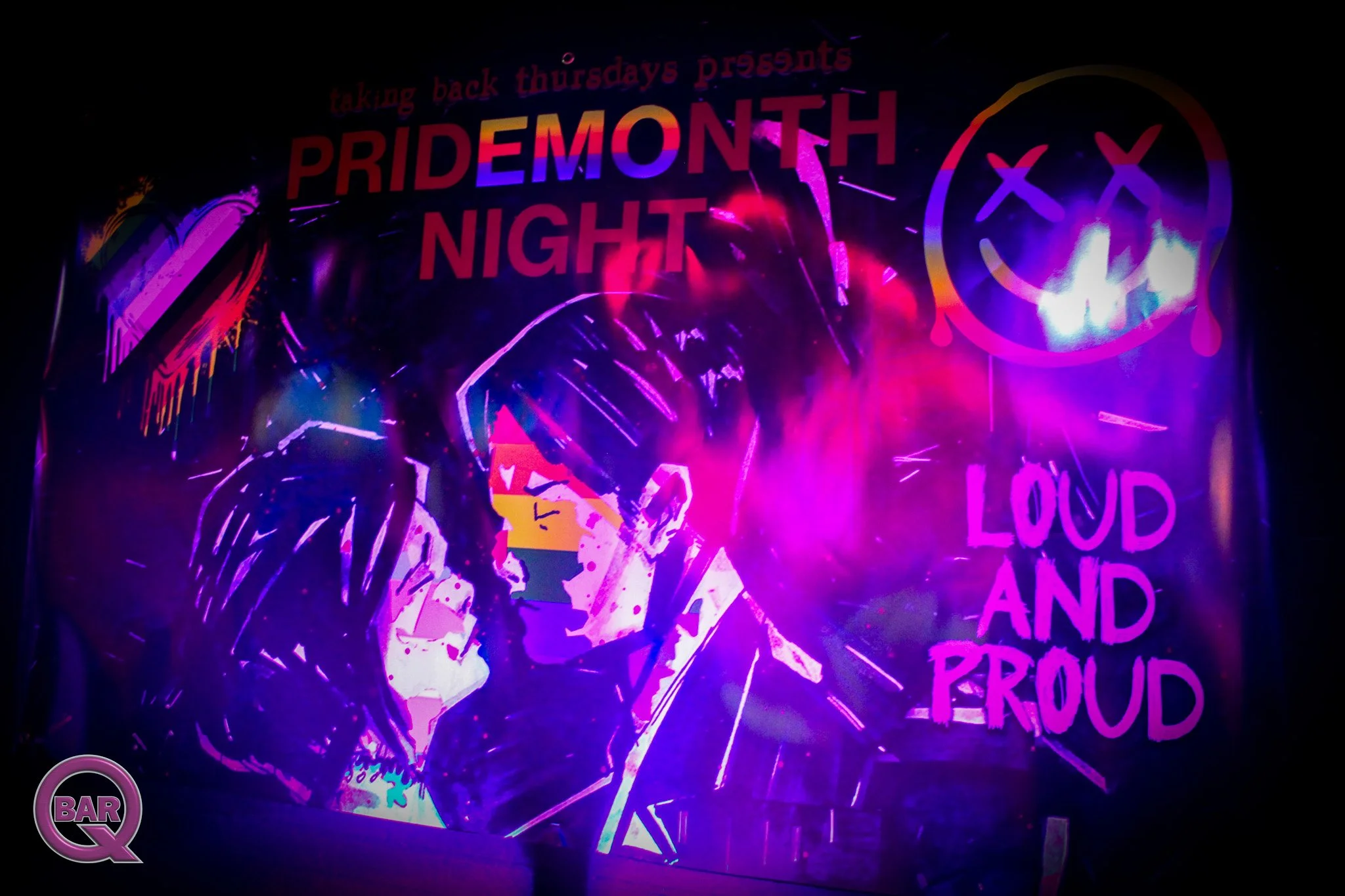 Colorful neon sign promoting Pride Month Night event with a smiley face and various words, including 'taking back thursdays presents.'