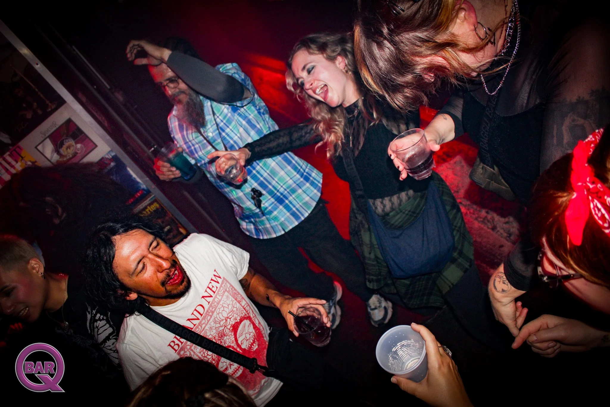 Group of people dancing and enjoying a night out at a bar or club, with some holding drinks and smiling.