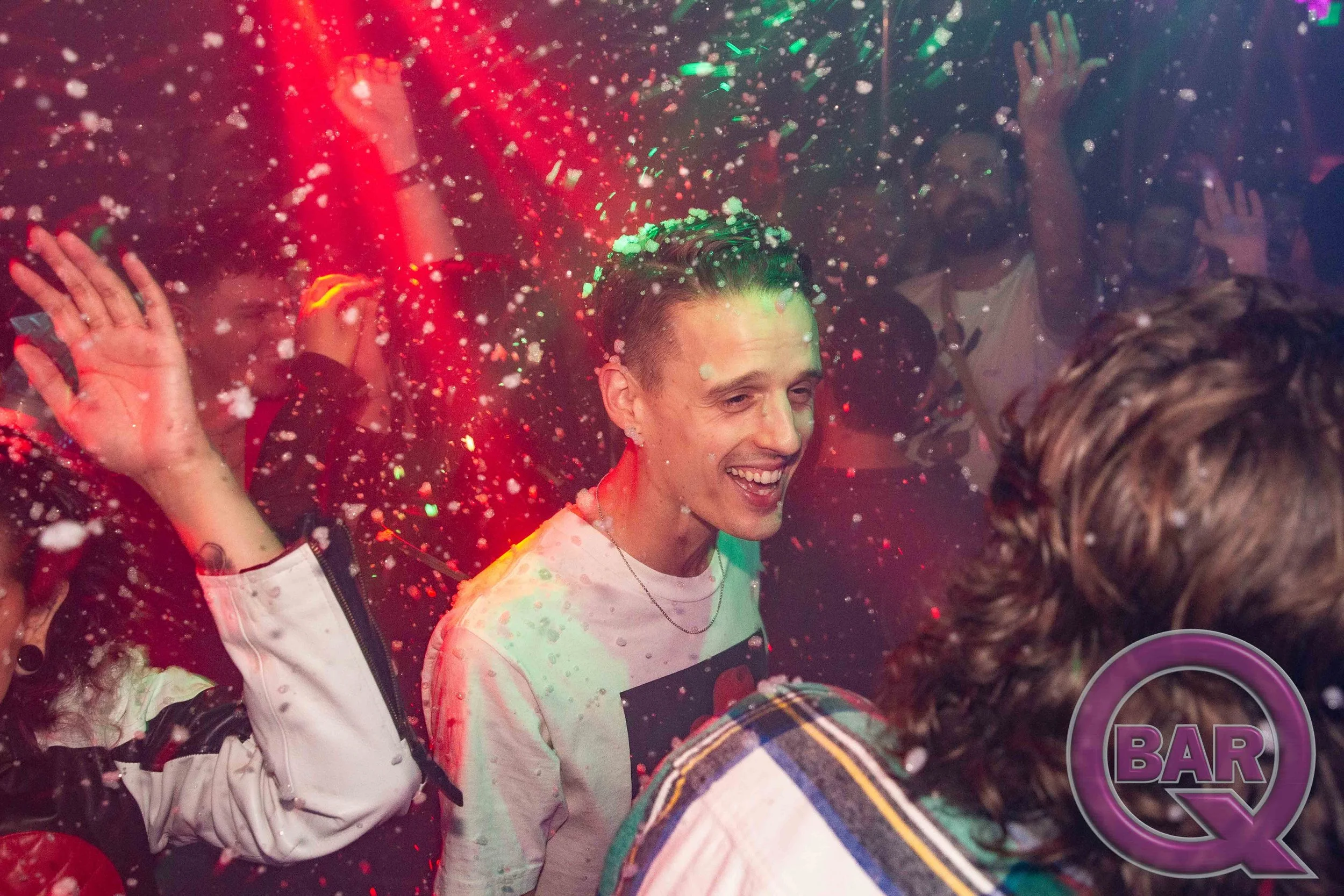 People celebrating at a bar with confetti and colorful lights, smiling and enjoying the party.