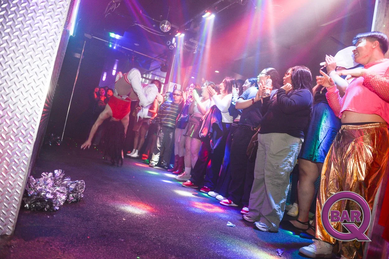 Audience watching a performer in drag performing on stage at a nightclub, with colorful lighting and a 'BAR Q' sign in the corner.