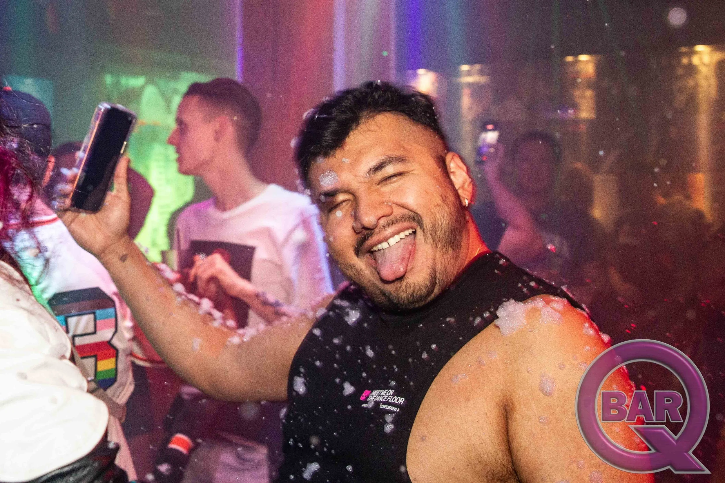 People celebrating at a foam party in a club, smiling and having fun while foam covers their bodies.