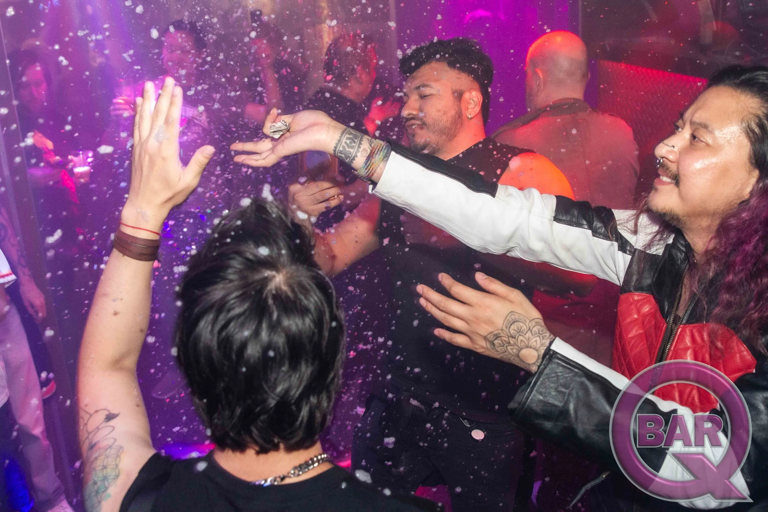 People celebrating at a bar with foam and colorful lights, high-fiving and smiling.