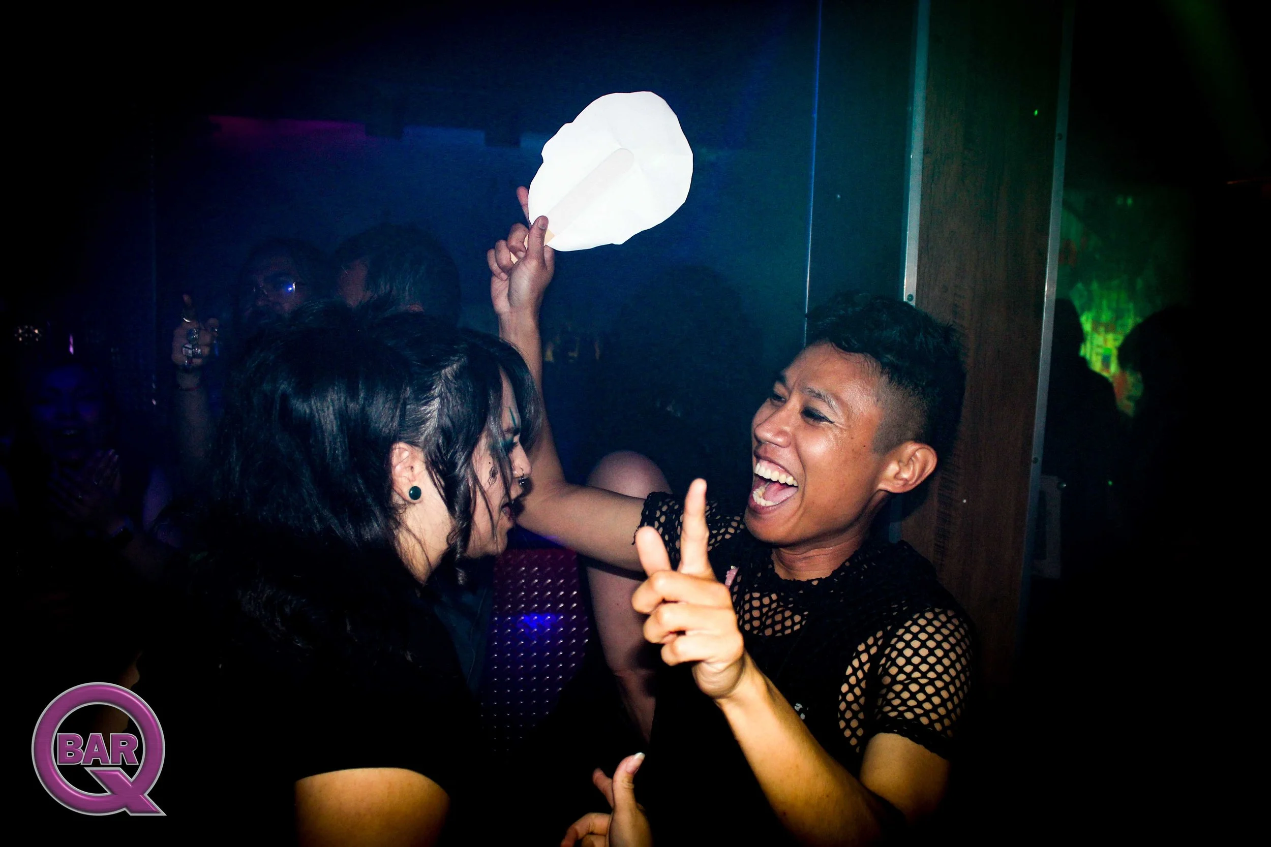 People dancing and having fun at a nightclub or bar. One person is holding a paper lantern, and others are smiling and enjoying the moment.