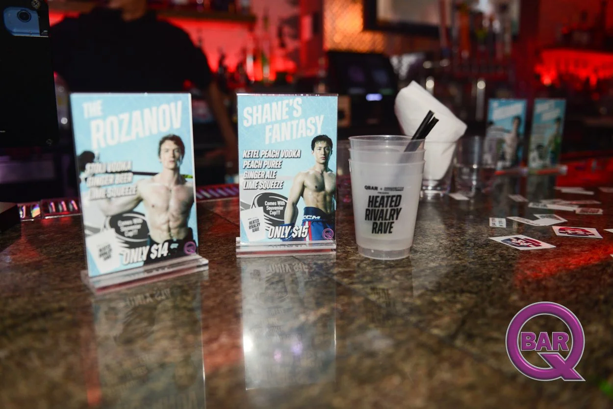 Promotional flyers for an event featuring Shane's Fantasy and The Rozanov, with a drink cup labeled 'Heated Rivalry Rave' on a bar counter. The flyers showcase a shirtless male model, and there are scattered playing cards on the counter, with a blurr