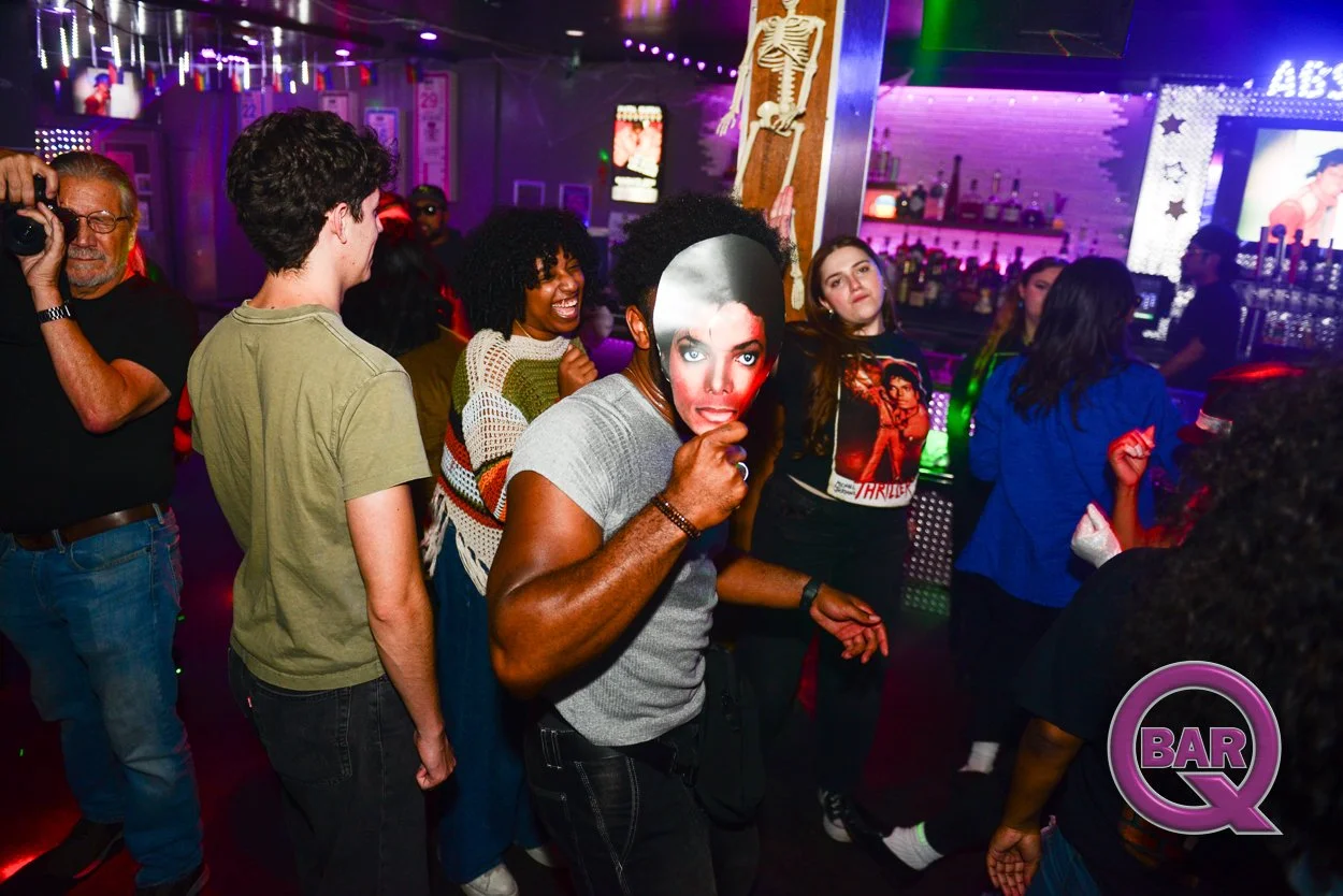 People dancing and socializing at a lively bar with colorful lights and a decorated interior.
