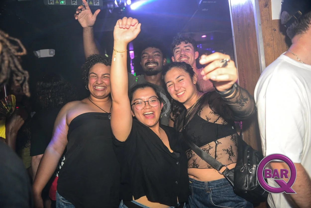 Group of five diverse friends celebrating and smiling at a bar or nightclub, with some raising their arms and showing expressions of joy and excitement.
