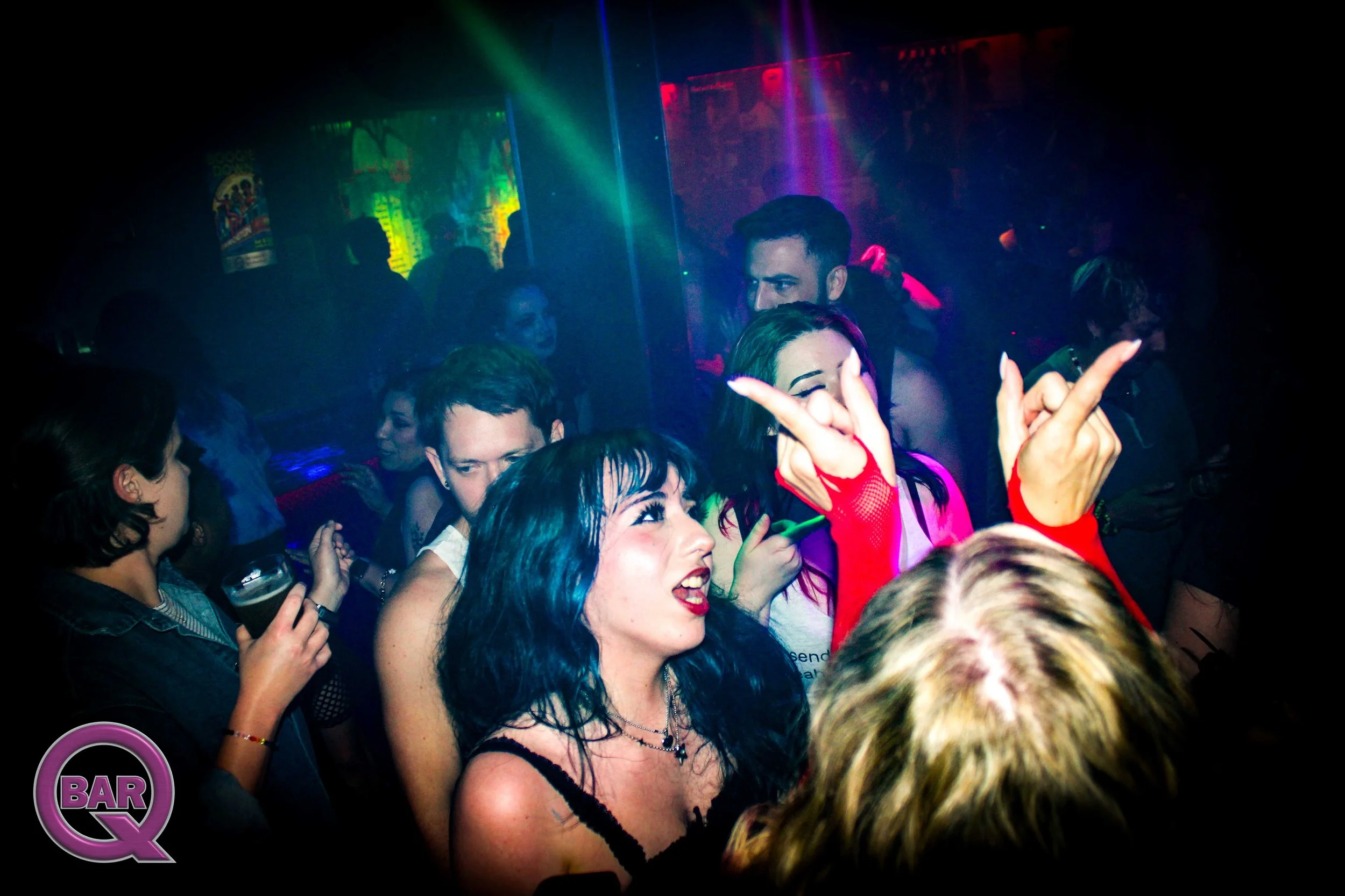 People dancing and celebrating in a nightclub with colorful lighting and a dark atmosphere.