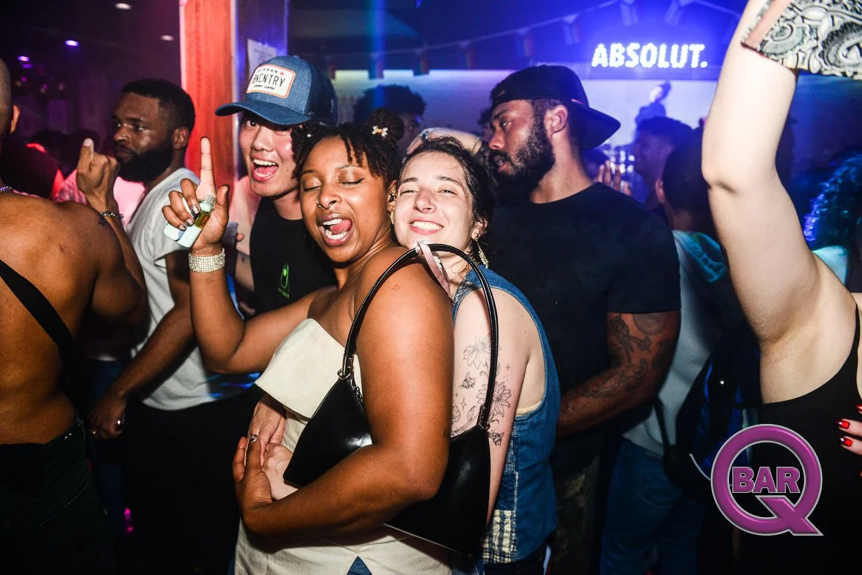 Group of diverse young adults dancing and enjoying themselves at a nightclub or party, with colorful lighting and a 'BAR Q' logo in the bottom right corner.