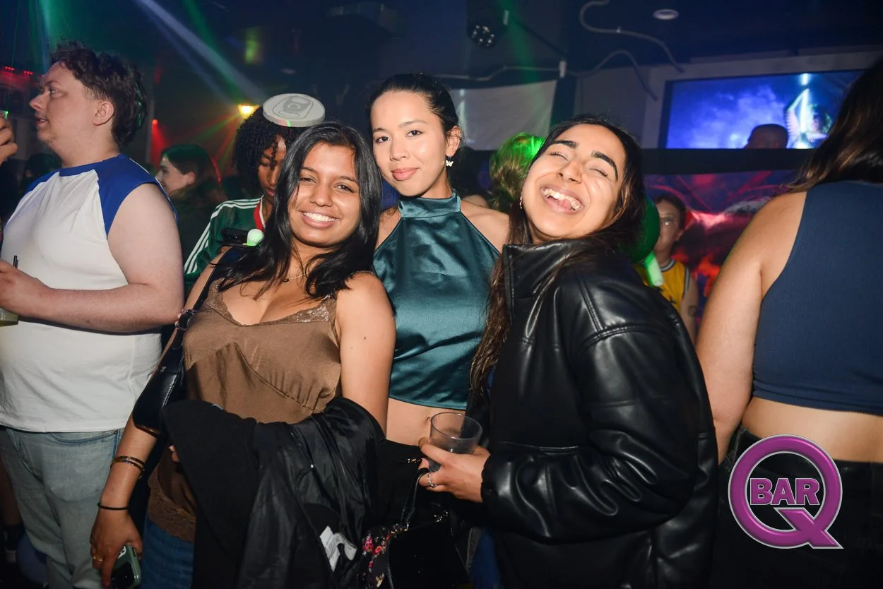 Group of people partying in a nightclub, smiling and enjoying drinks with colorful lights and screens in the background.