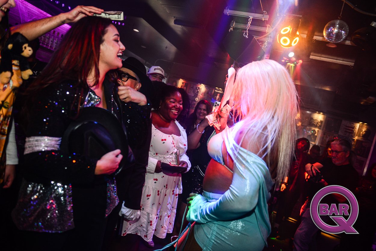 People dancing and having fun at a nightclub with colorful lighting, including a woman with platinum blonde hair in front of others who are smiling and enjoying the music.