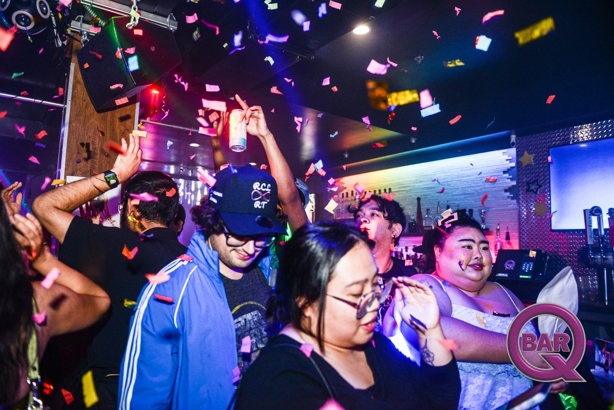 People dancing and celebrating in a nightclub with colorful confetti falling from the ceiling.