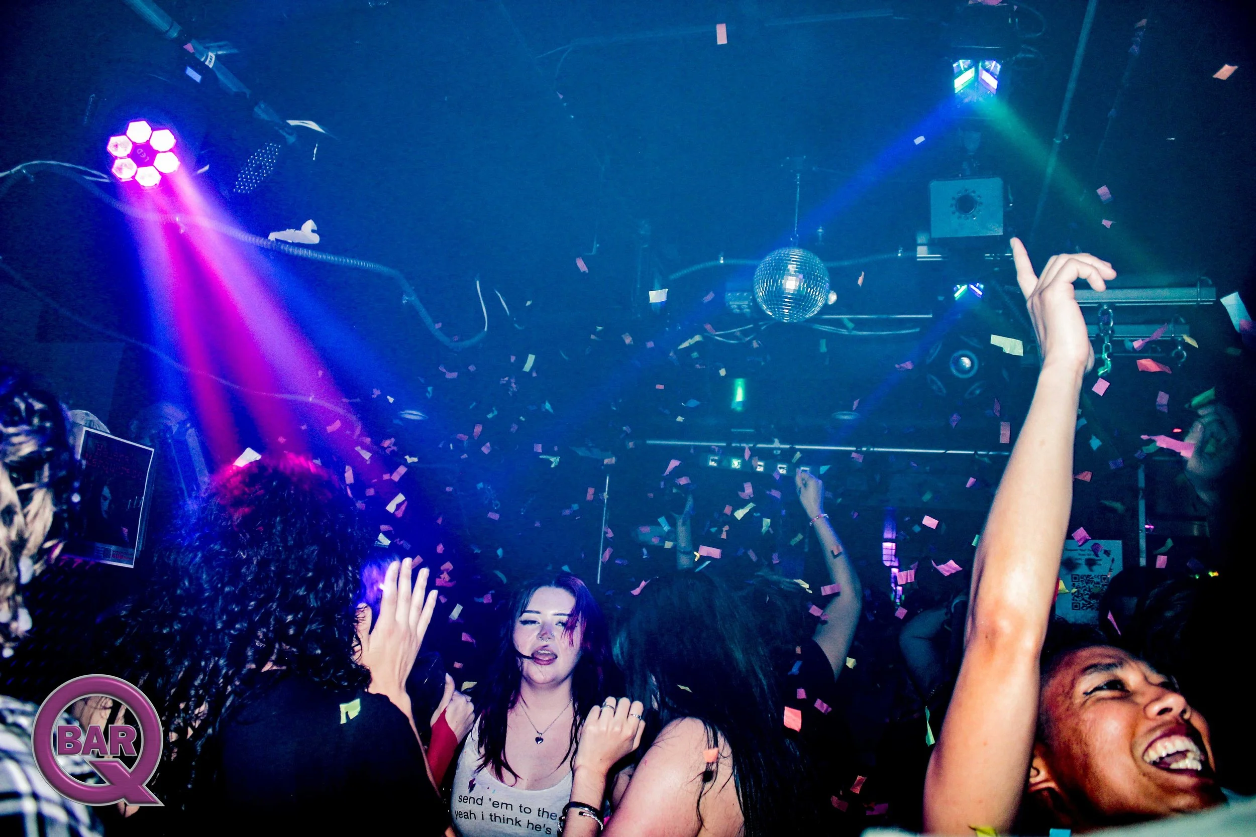 People dancing and celebrating in a nightclub or concert venue with colorful lights and confetti.