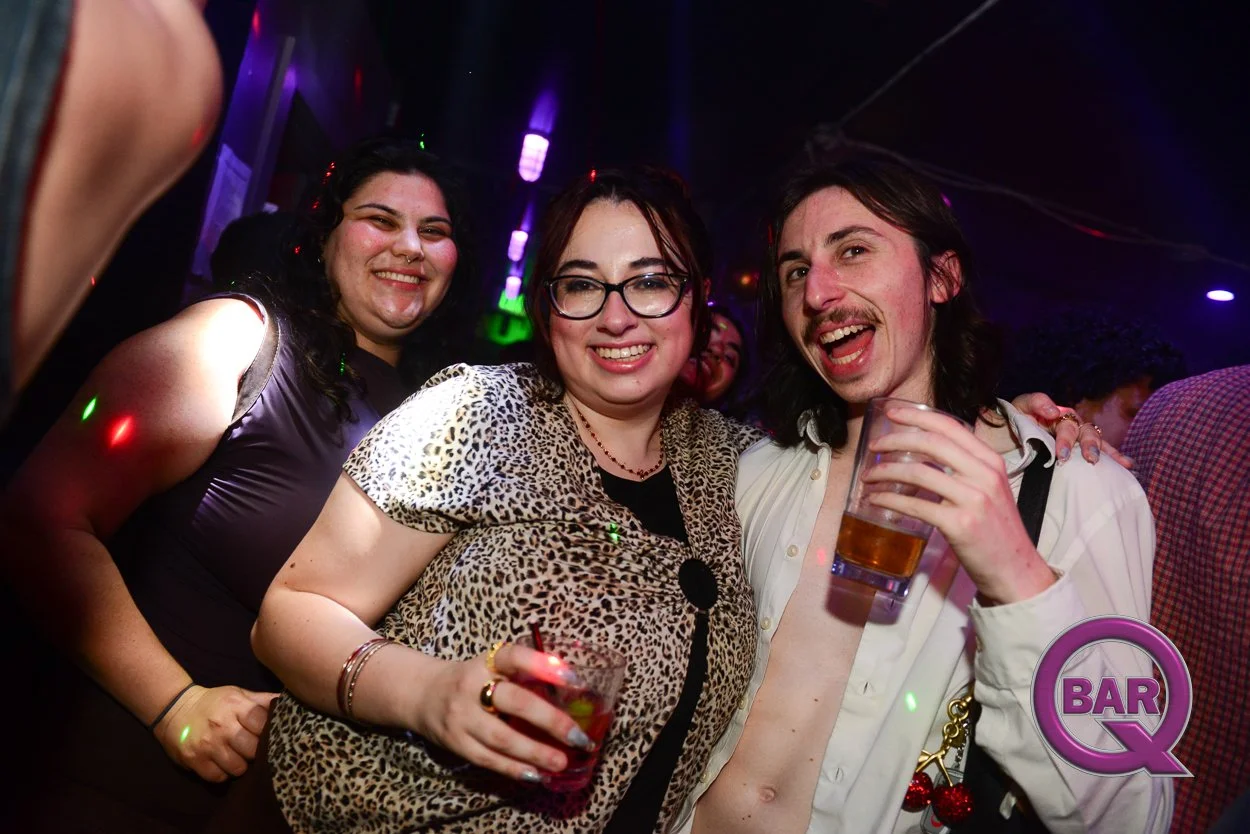 Three friends enjoying drinks and dancing at a lively bar or nightclub.