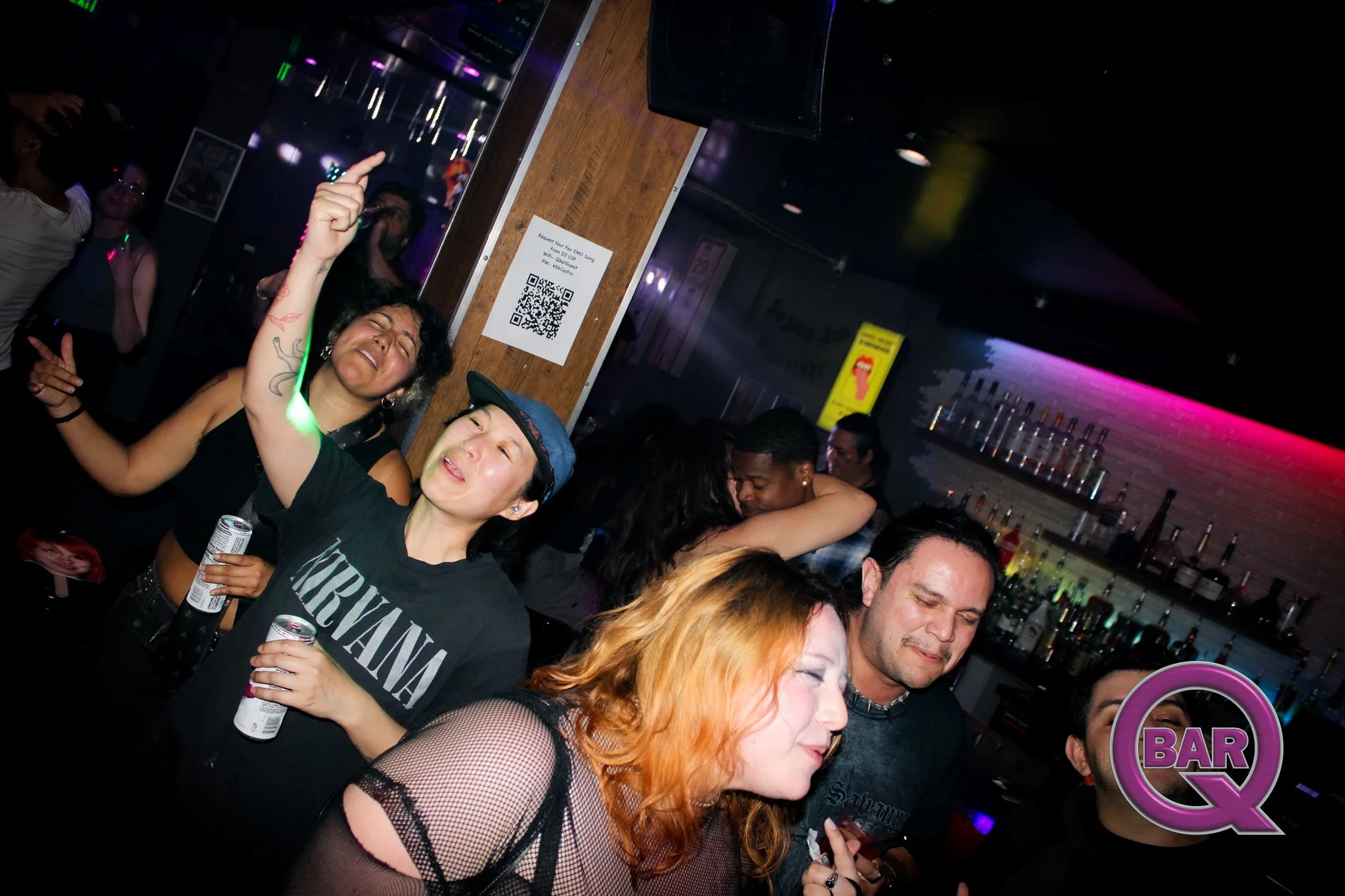 People dancing and enjoying themselves at a bar or nightclub with neon lighting and a bar counter in the background.