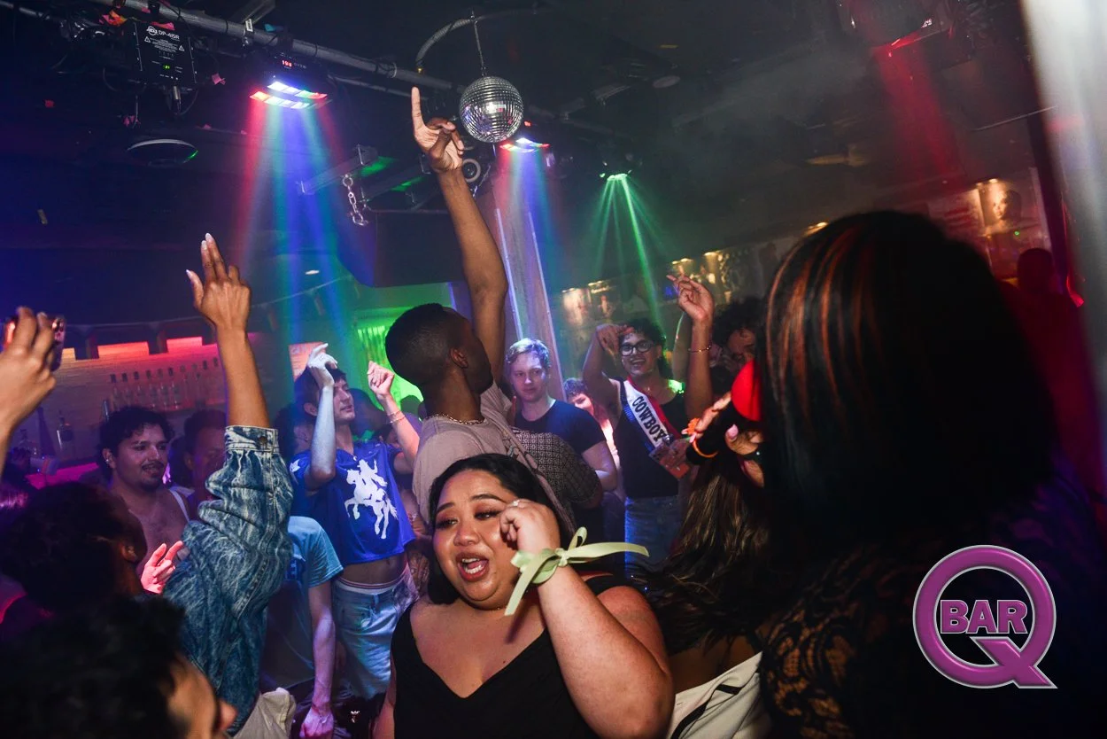 People dancing and enjoying at a nightclub with colorful lights and a disco ball, with a woman in the foreground wiping her eyes and others smiling and raising their hands.