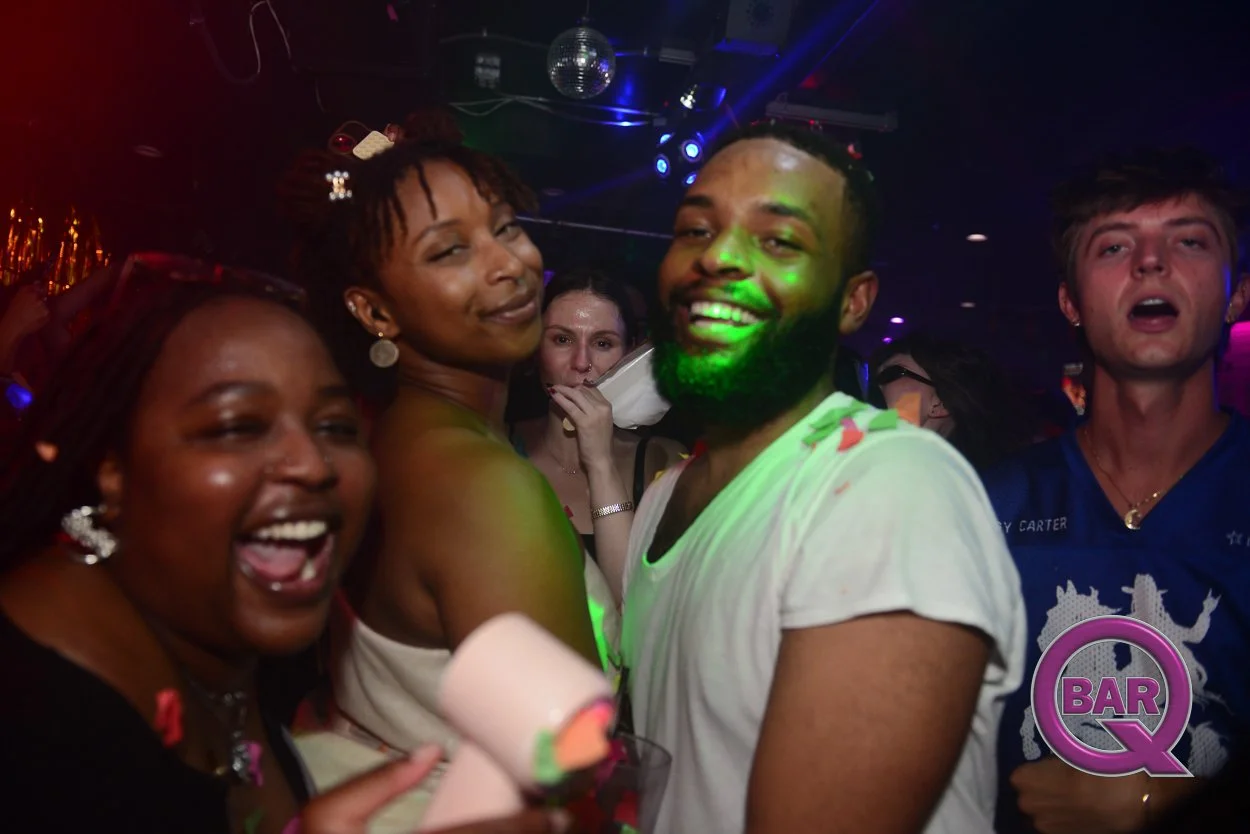 Group of people dancing and smiling at a nightclub or party, with colorful lights and a disco ball