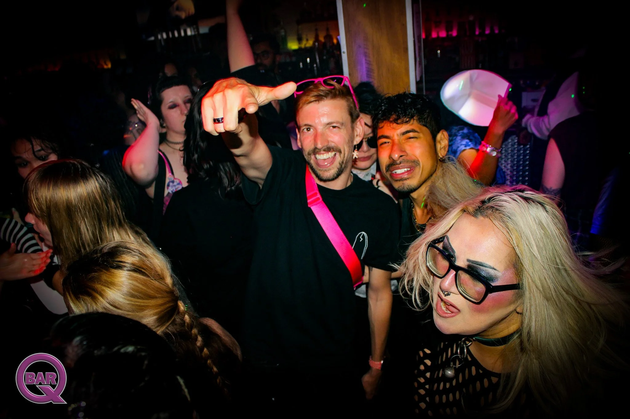People dancing and having fun at a bar or nightclub with colorful lighting, smiling, and enjoying the party atmosphere.