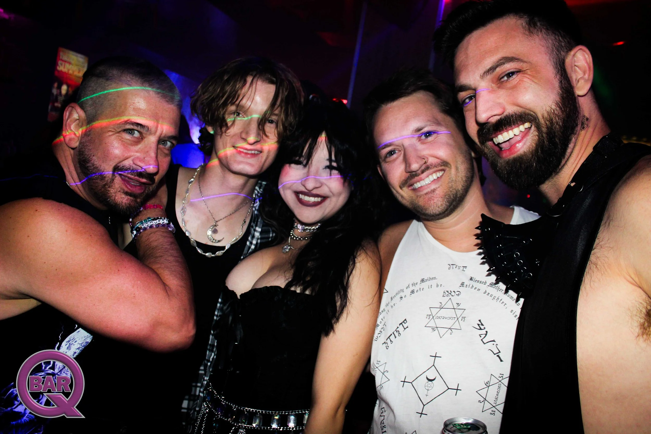 Group of five smiling friends taking a selfie at a party or club with dark background and neon lights.