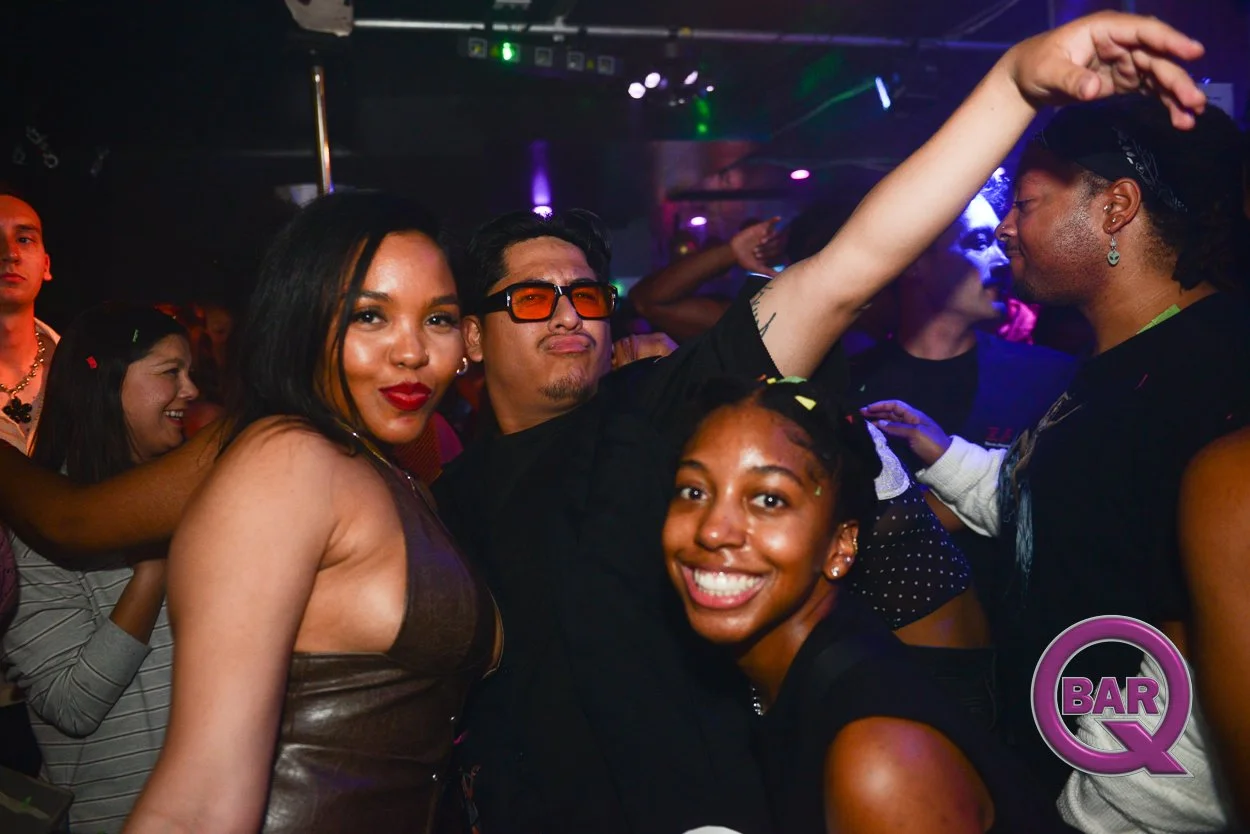 People dancing and having fun at a nightclub, with a woman smiling in the foreground and others enjoying the music.