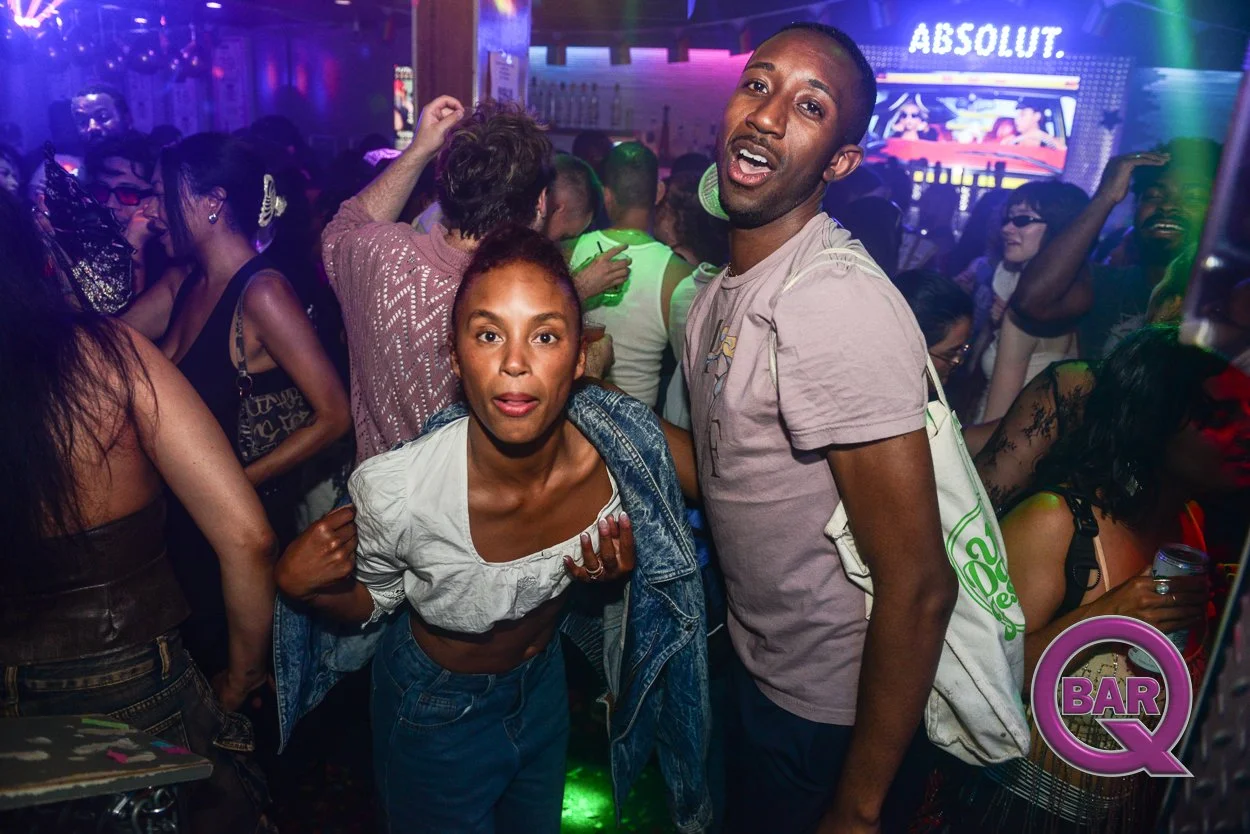 A crowded nightclub dance floor with diverse people dancing and socializing under colorful lights, with a bar and a screen displaying the word 'ABSOLUT' in the background.