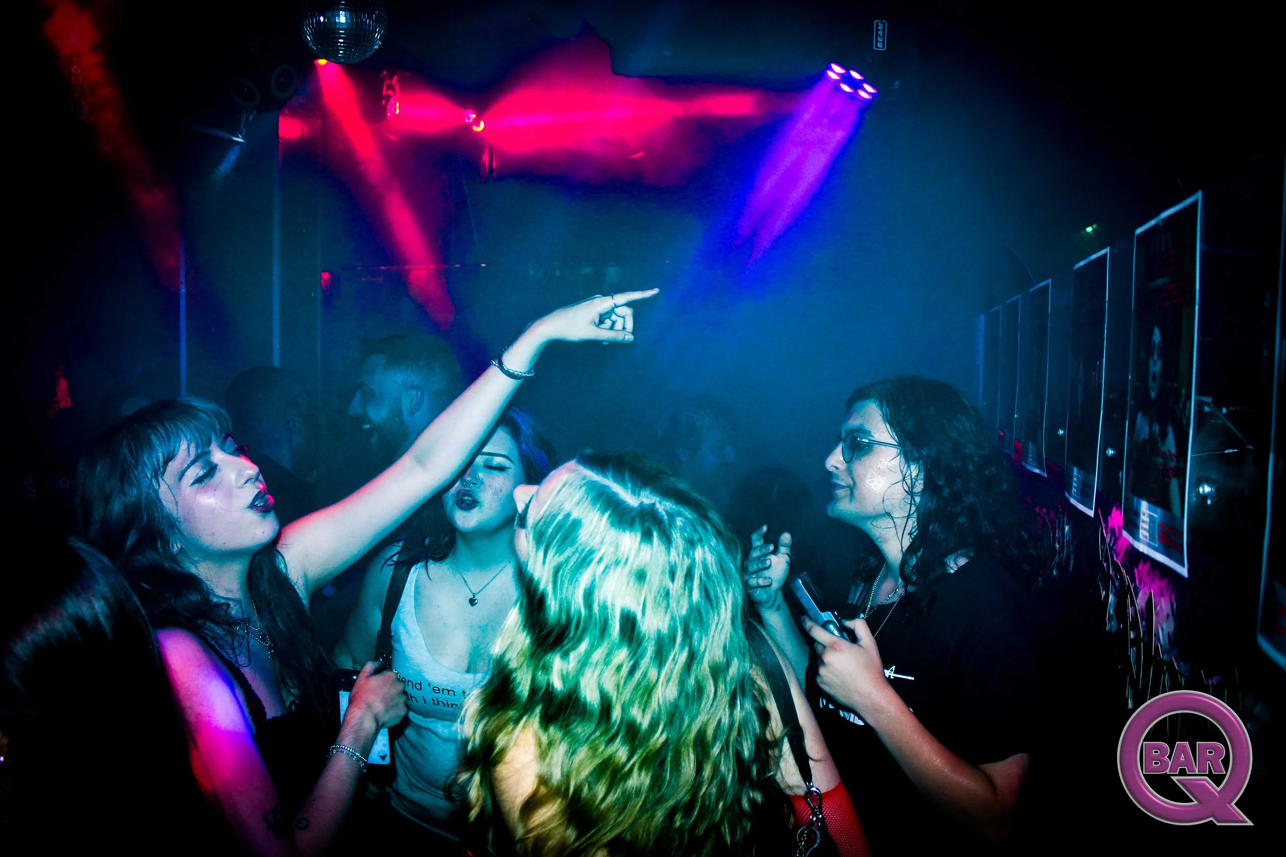 A group of women dancing and socializing in a nightclub with colorful lights and a disco ball.