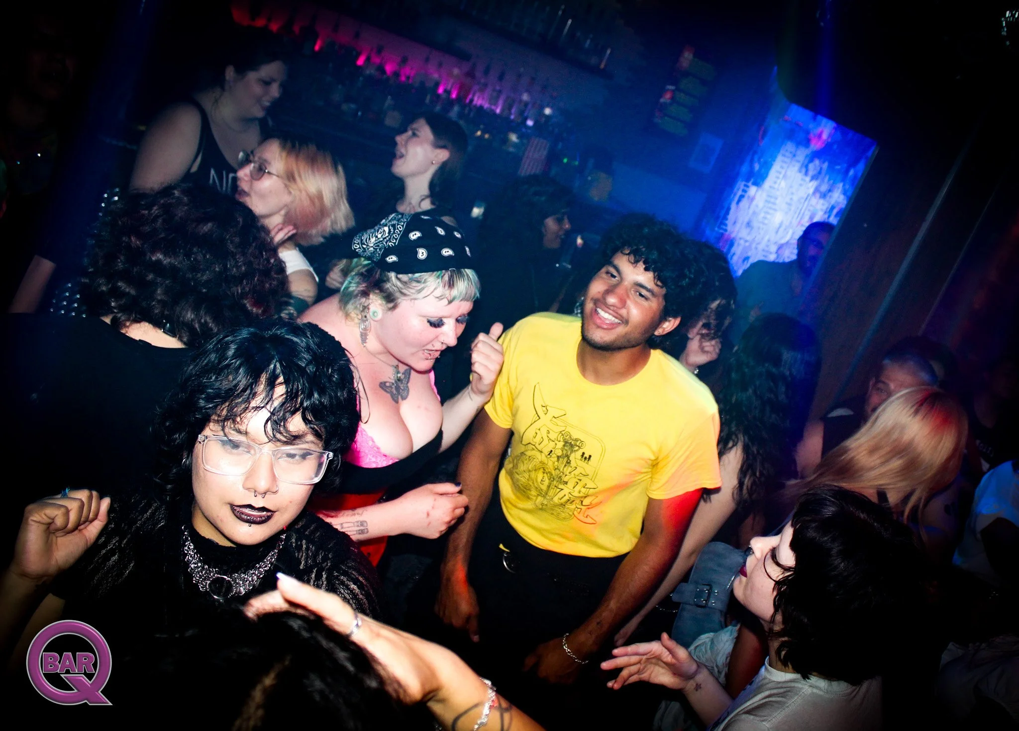 People dancing and socializing in a nightclub with colorful lighting and a large screen in the background.