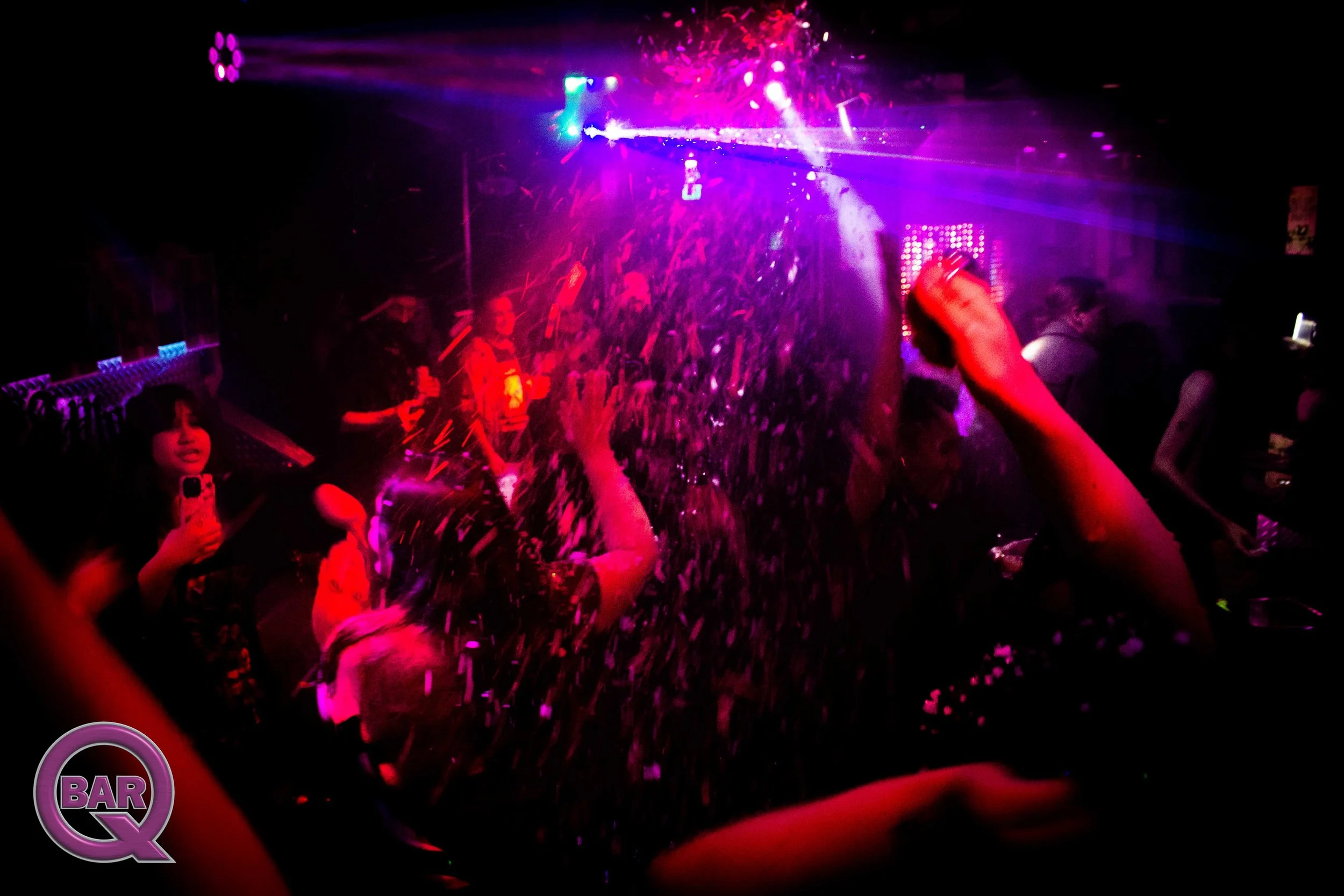 People dancing and having fun at a nightclub with colorful lights, confetti, and laser effects.