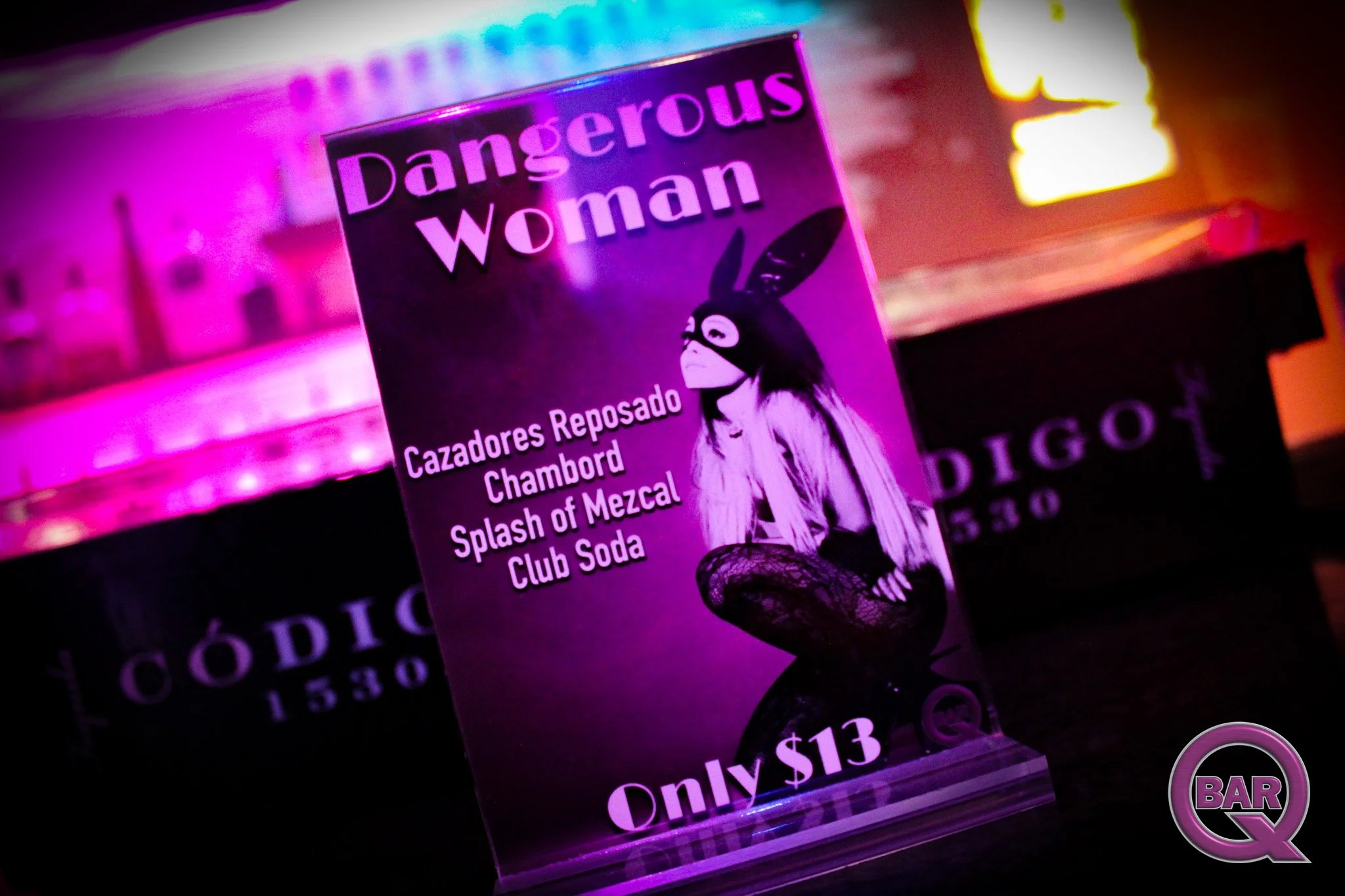 A close-up of a neon-lit sign with a purple and pink color scheme displaying a woman in a mask and bunny costume, and text that reads 'Dangerous Woman' and 'Only $13'.