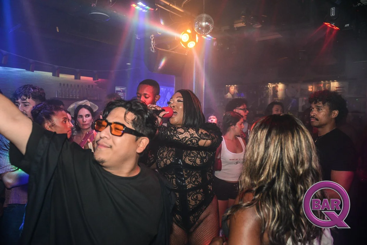 People dancing and having fun in a nightclub with colorful lights and a disco ball, with a woman singing into a microphone.