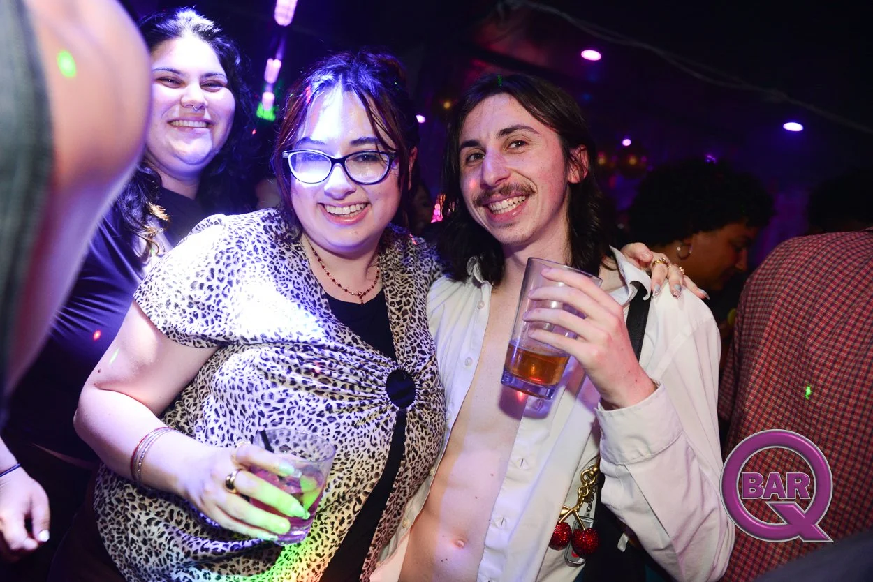 Group of three friends enjoying drinks at a bar or nightclub, with colorful lighting and festive atmosphere.