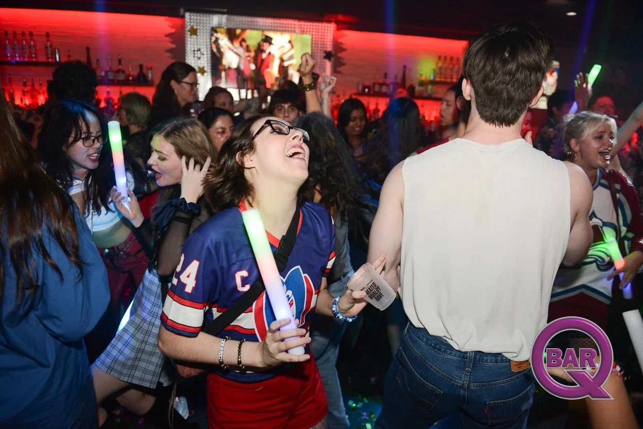 People dancing and celebrating at a lively nightclub with colorful lights, holding glow sticks, and smiling.