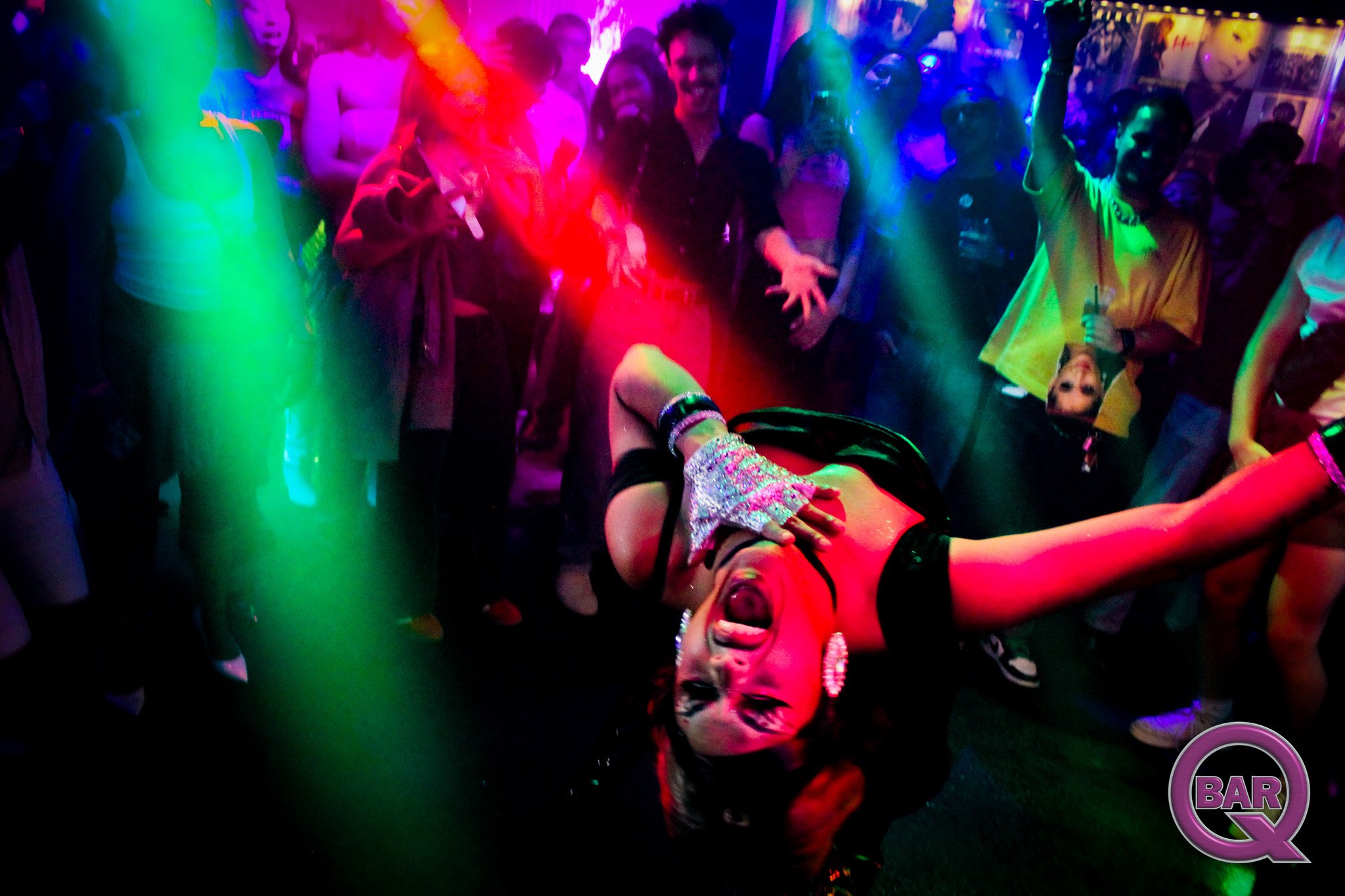 People dancing and celebrating in a nightclub with colorful neon lighting.