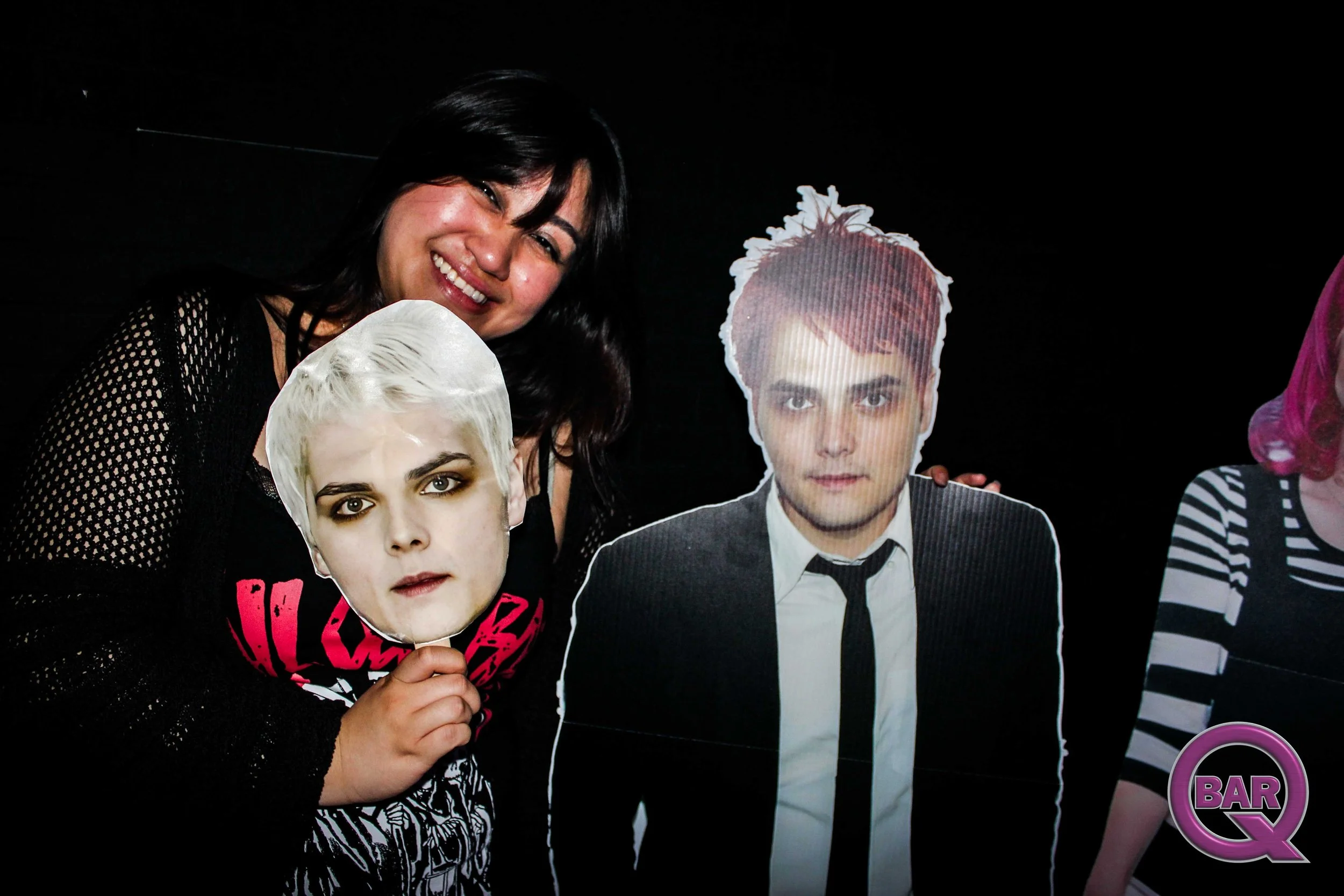 Woman smiling with black hair holding a cardboard cutout of a man's face at a night event.