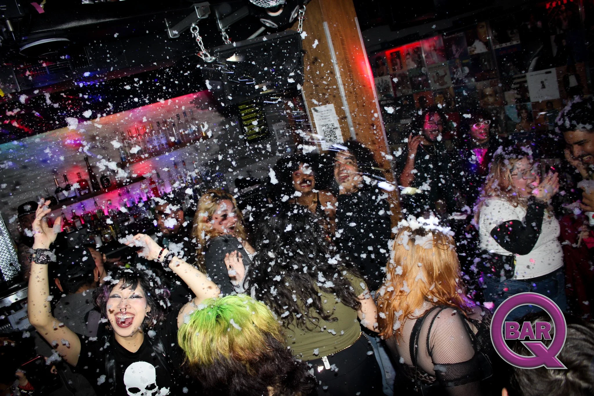 People dancing and celebrating with foam in a crowded nightclub or bar with colorful lighting.