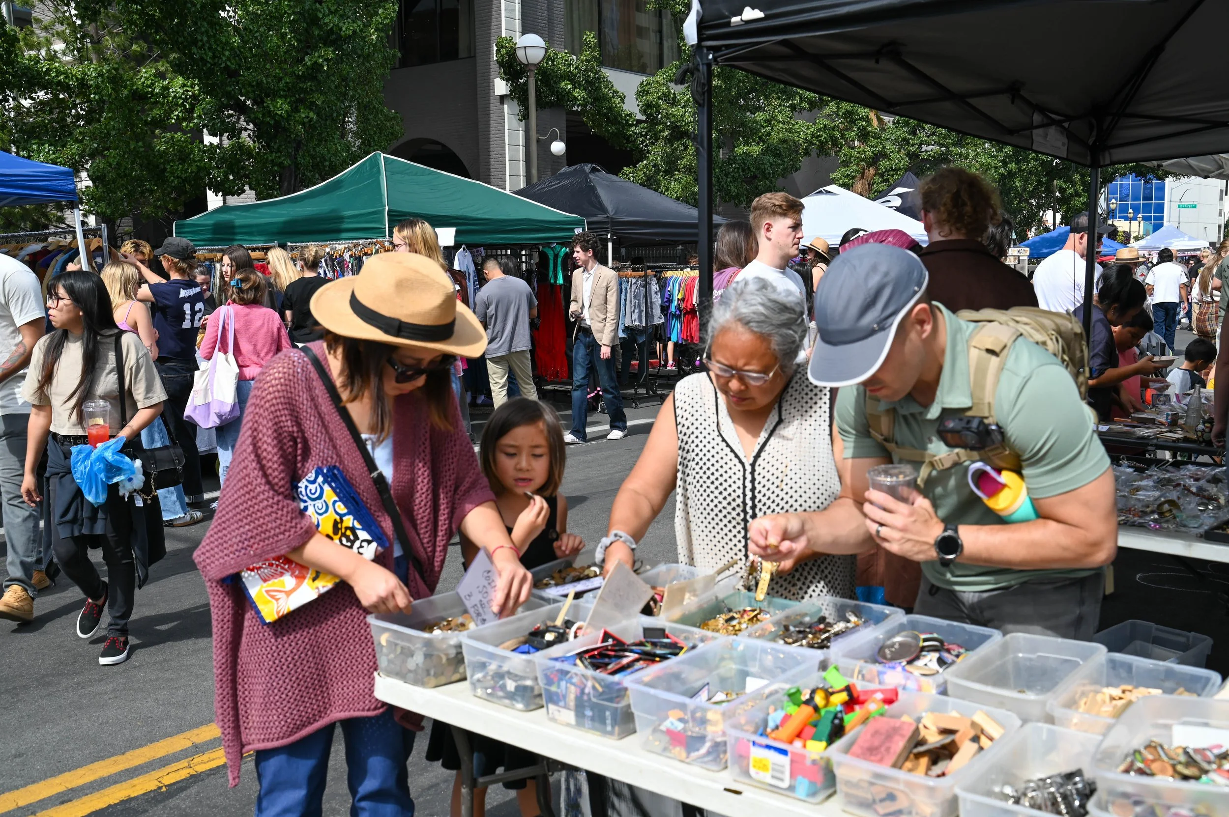 A family spanning generations, from a young child to an elderly relative, gathers around a table of small collectibles, each searching through the trays in their own way.