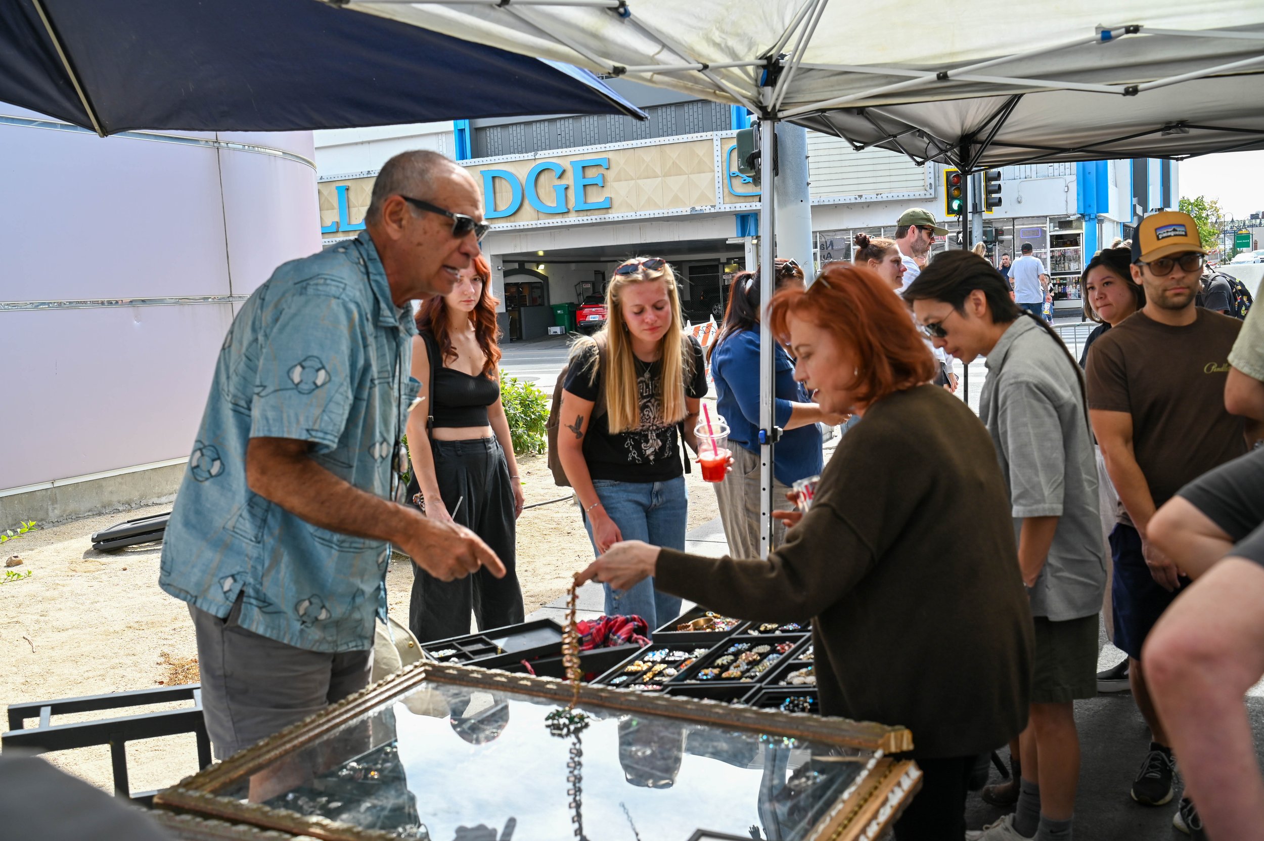 A shopper asks the vendor about the price of an antique jewelry piece as she considers buying it.