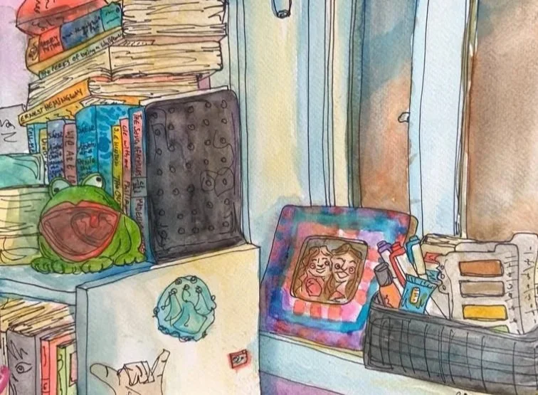 Watercolor illustration of a cluttered desk with a frog plush toy, a pile of books, a framed photo of two smiling people, a black container filled with various office supplies, and a window in the background.
