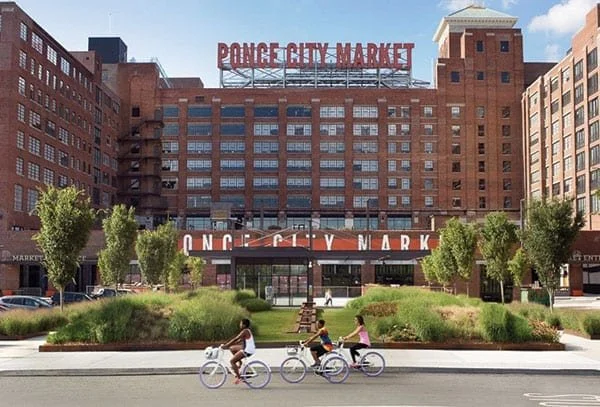People riding bikes in front of Ponce City Market, a large brick building with a sign on top.