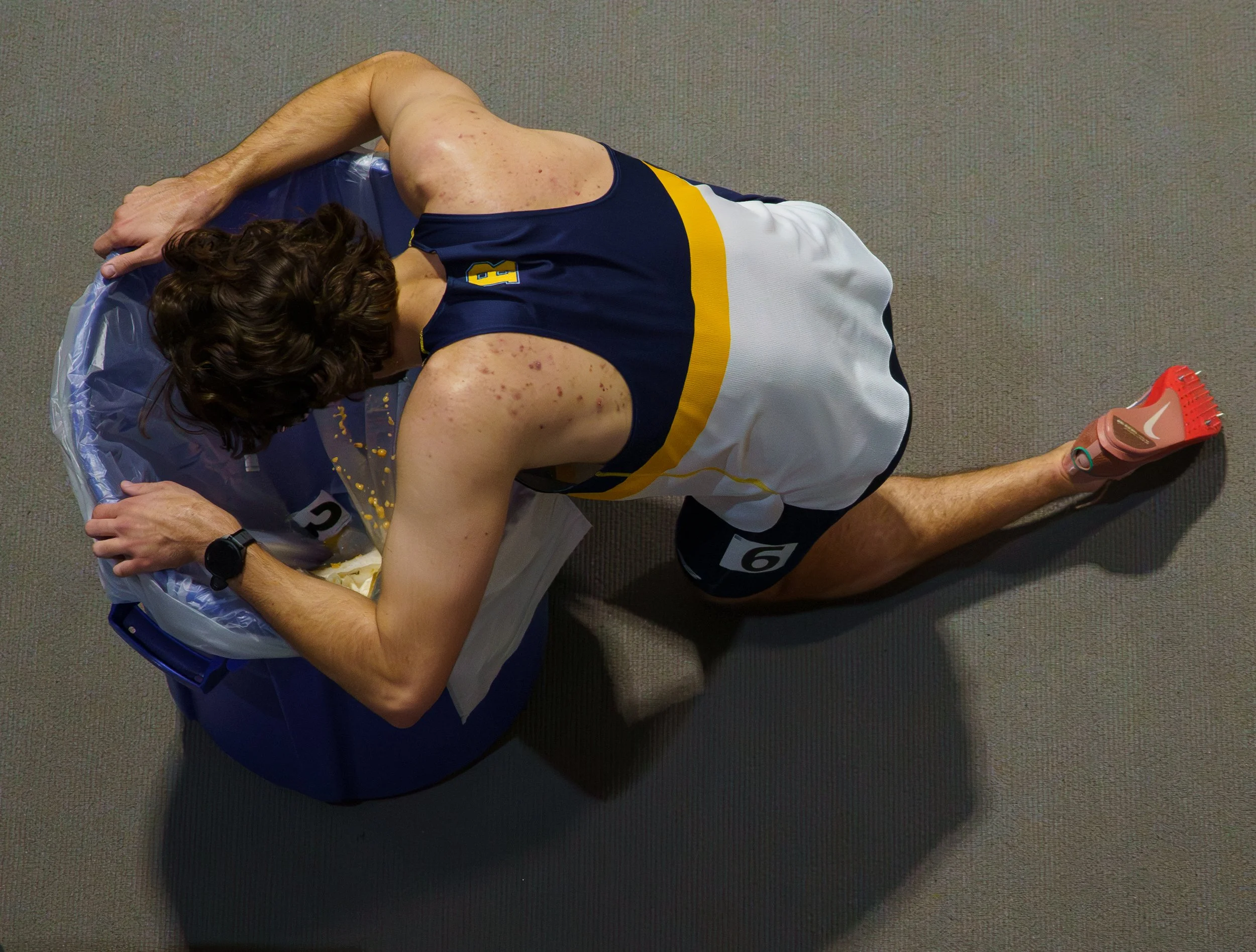Brendan McCollum vomits in a trash can after running in the Men’s 500m Final at the Nazareth University Alumni Meet at Golisano Training Center on Dec. 5, 2025 in Rochester, N.Y. McCollum finished second with a final time of 1:06.65.