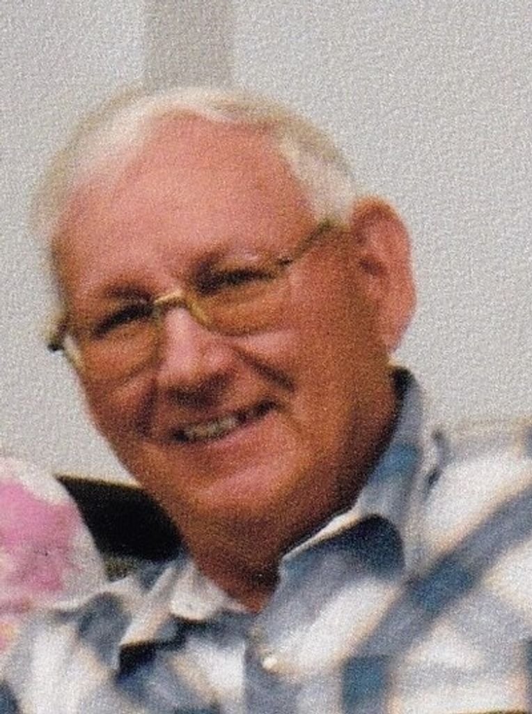 A smiling elderly man with white hair, wearing glasses and a plaid shirt.