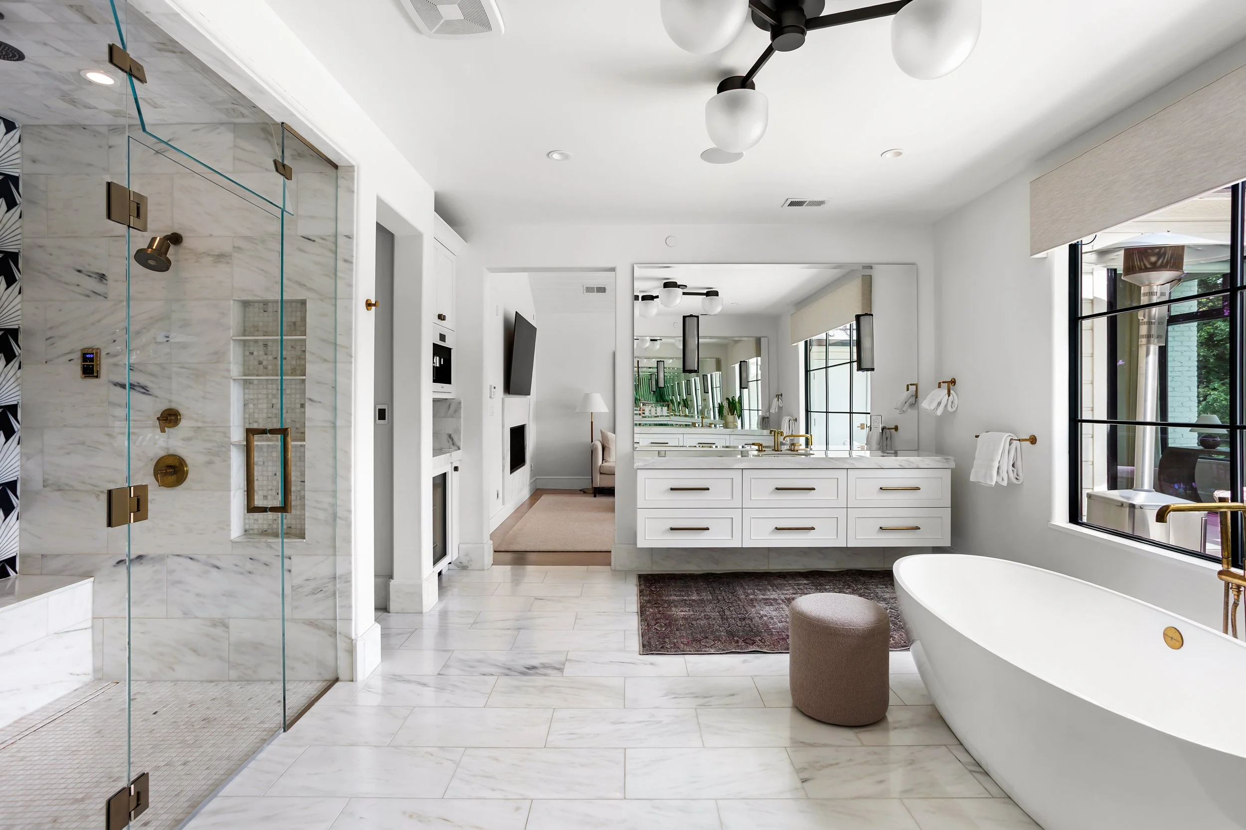 Modern bathroom with marble flooring, walk-in shower with glass door, white bathtub, large windows, and minimalist design.