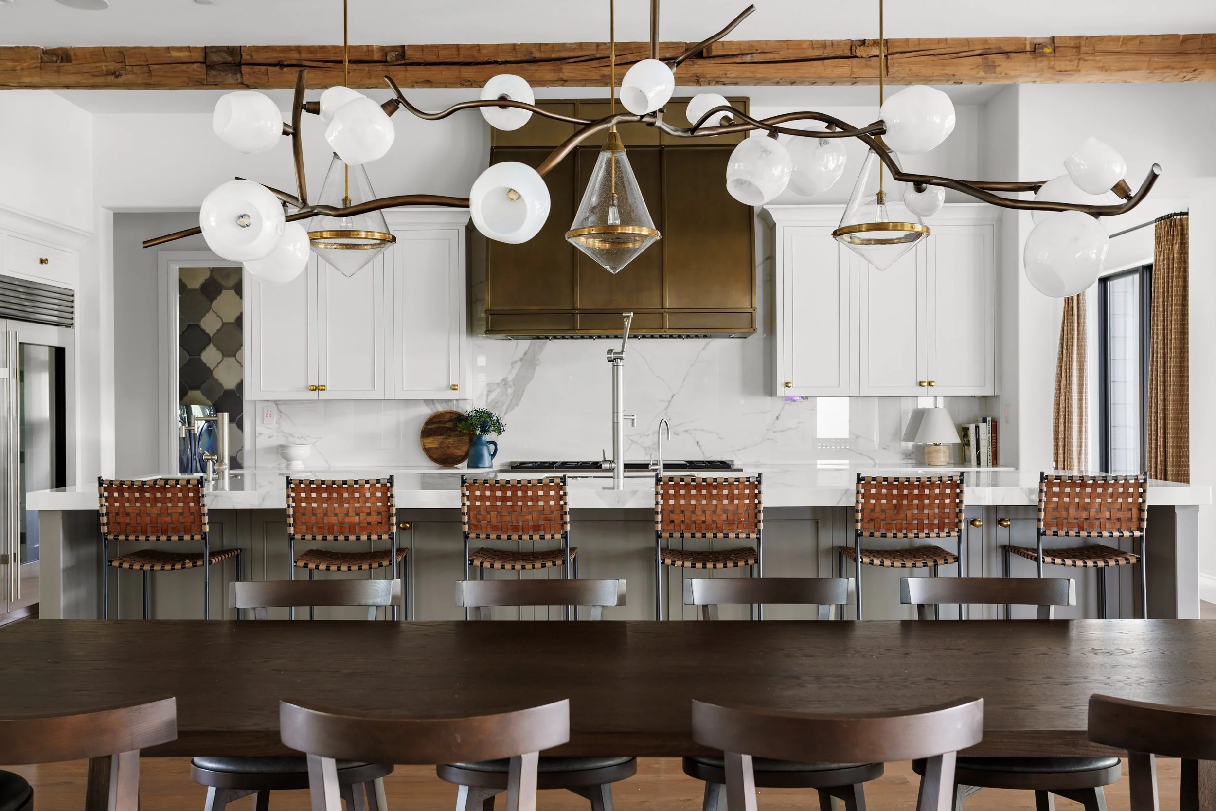 Modern kitchen with a large island, white cabinets, brass hardware, a range hood, and a unique chandelier with white globes.